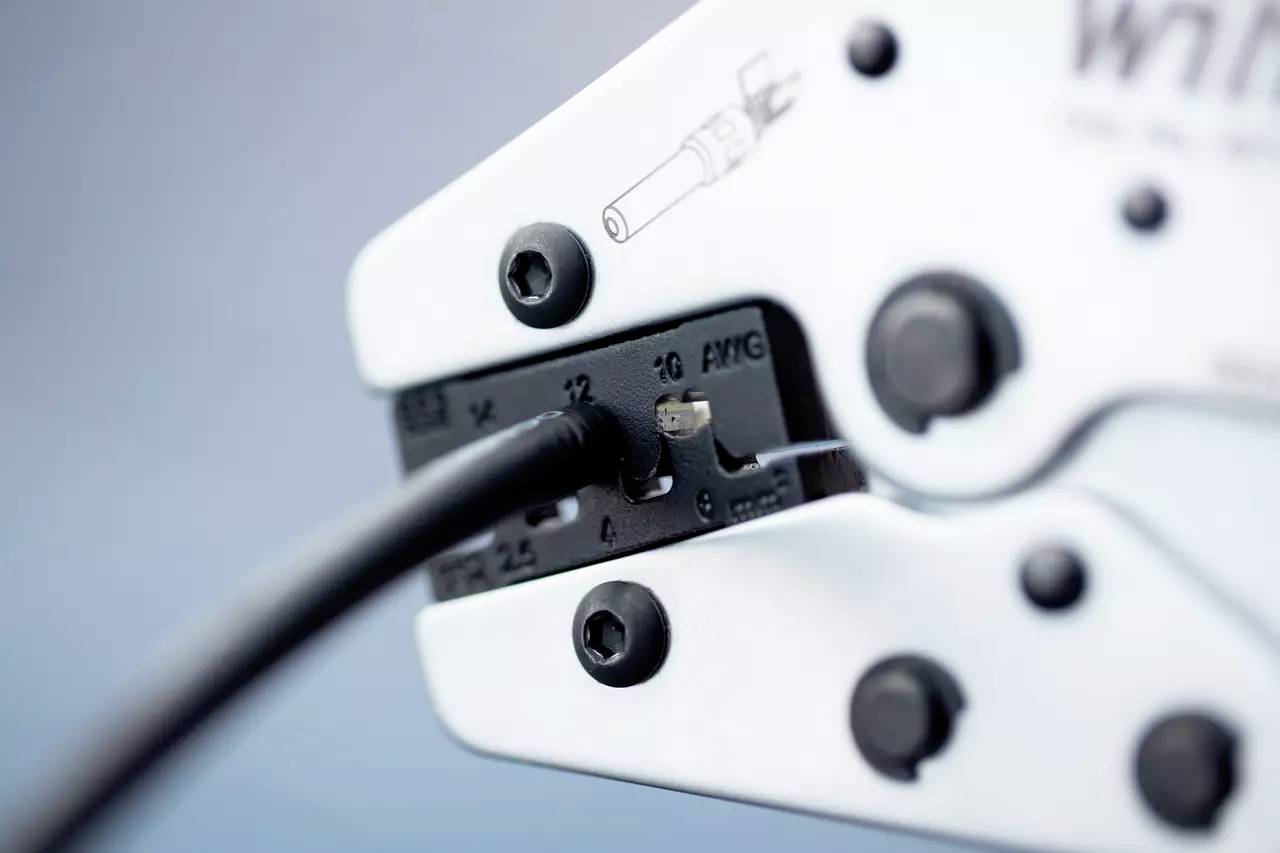 Nahaufnahme einer Crimpzange, die ein Kabel verarbeitet. Die Zange hat Markierungen für verschiedene Kabelgrößen.
