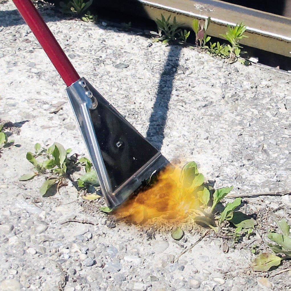 Ein Unkrautbrenner mit rotem Griff wird verwendet, um Unkraut auf einem Gehweg mit Flammen zu entfernen.