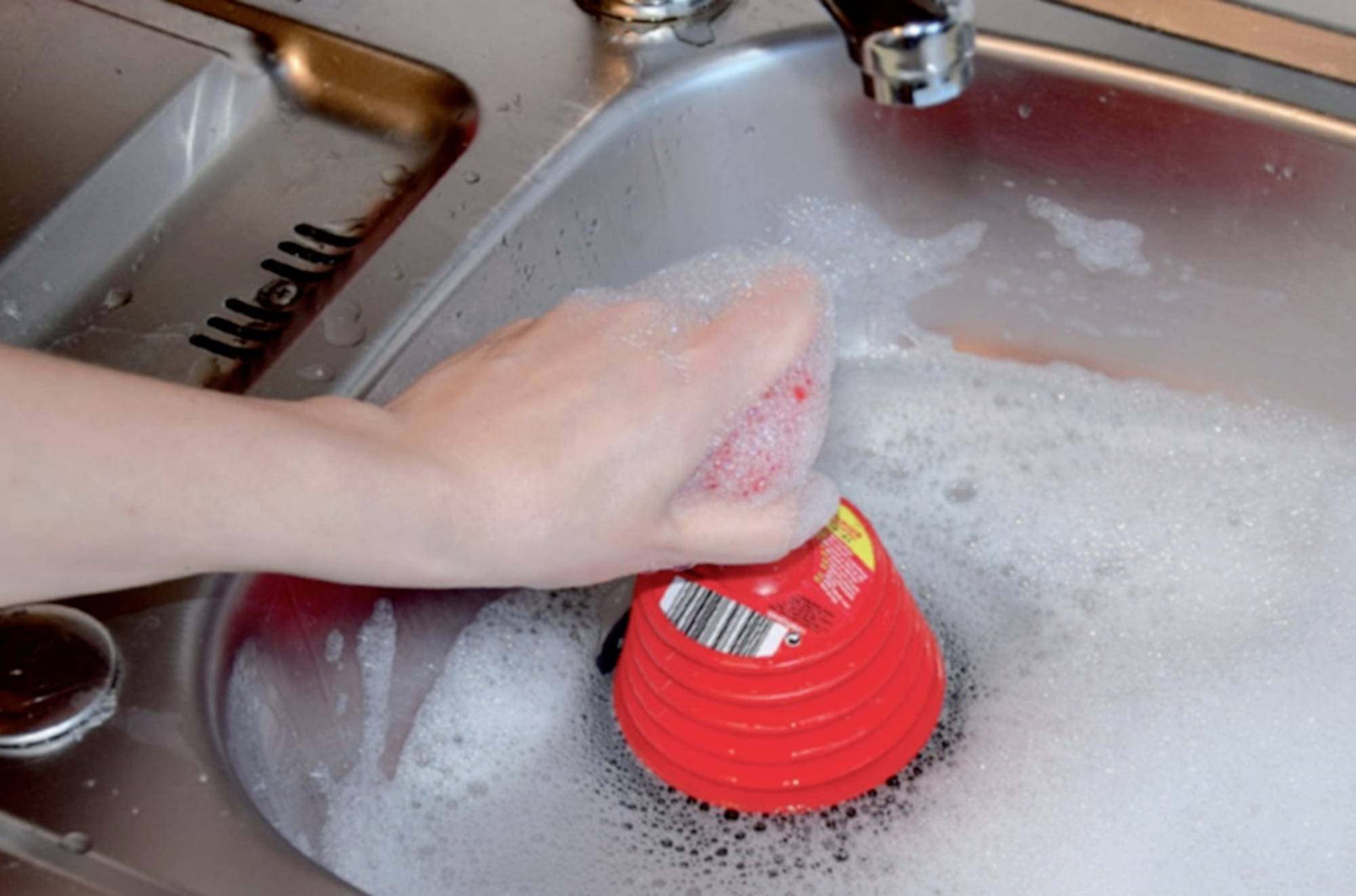 Eine Hand wäscht eine rote Schüssel mit Seifenwasser in einem Spülbecken. Bubbles sind zu sehen.