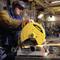 Ein mit Schutzkleidung ausgestatteter Arbeiter schneidet mit einer DeWalt-Maschine ein Metallrohr in einer industriellen Werkstattumgebung.