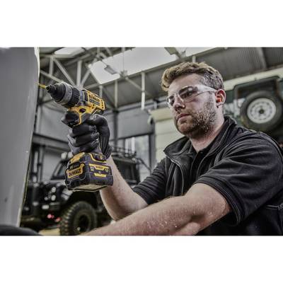 Mann benutzt einen Akku-Bohrschrauber in einer Werkstatt. Er trägt Schutzbrille. Im Hintergrund sind Werkstattdetails und ein Geländewagen sichtbar.