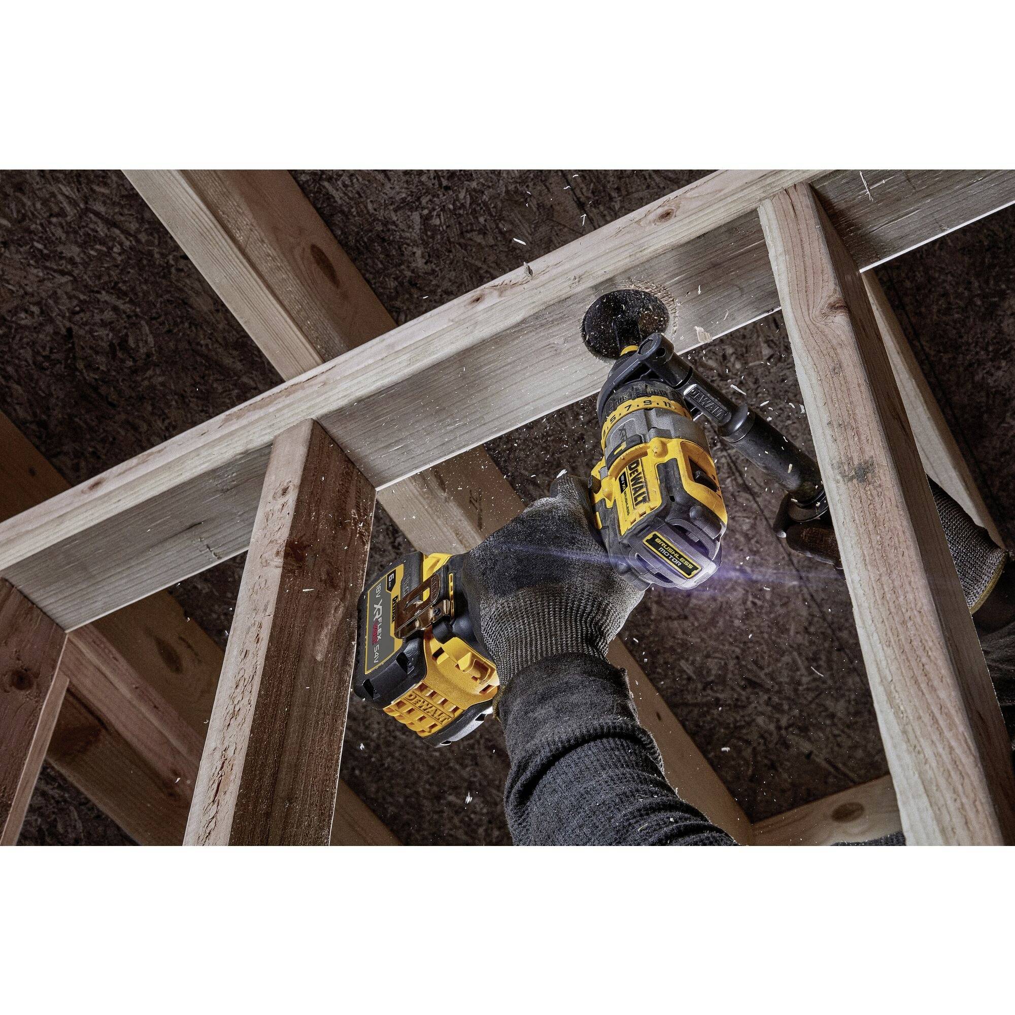 Eine Person bohrt mit einem Akkubohrer ein Loch in einen Holzrahmen. Sägespäne fliegen. Es wird an einem Dachstuhl gearbeitet.