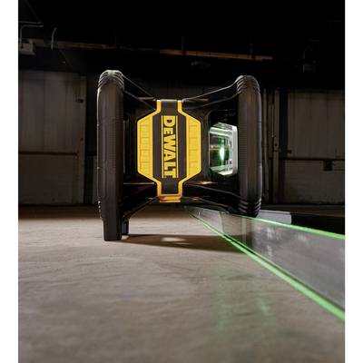 Ein gelbes und schwarzes Laser-Messgerät steht waagrecht auf dem Boden in einem leeren Raum. Ein grüner Laserstrahl leuchtet seitlich.