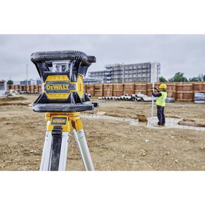 'Bauarbeiter benutzt Laser-Werkzeug auf Baustelle; unscharfer Hintergrund zeigt Holzstapel und Gebäude im Bau.'