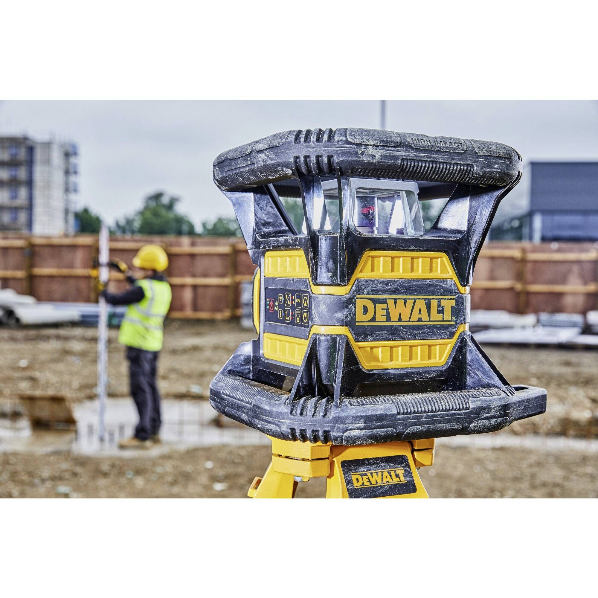 Ein Bauarbeiter misst auf einer Baustelle mit einem Vermessungsgerät im Vordergrund. DeWalt-Logo deutlich sichtbar auf dem Gerät.