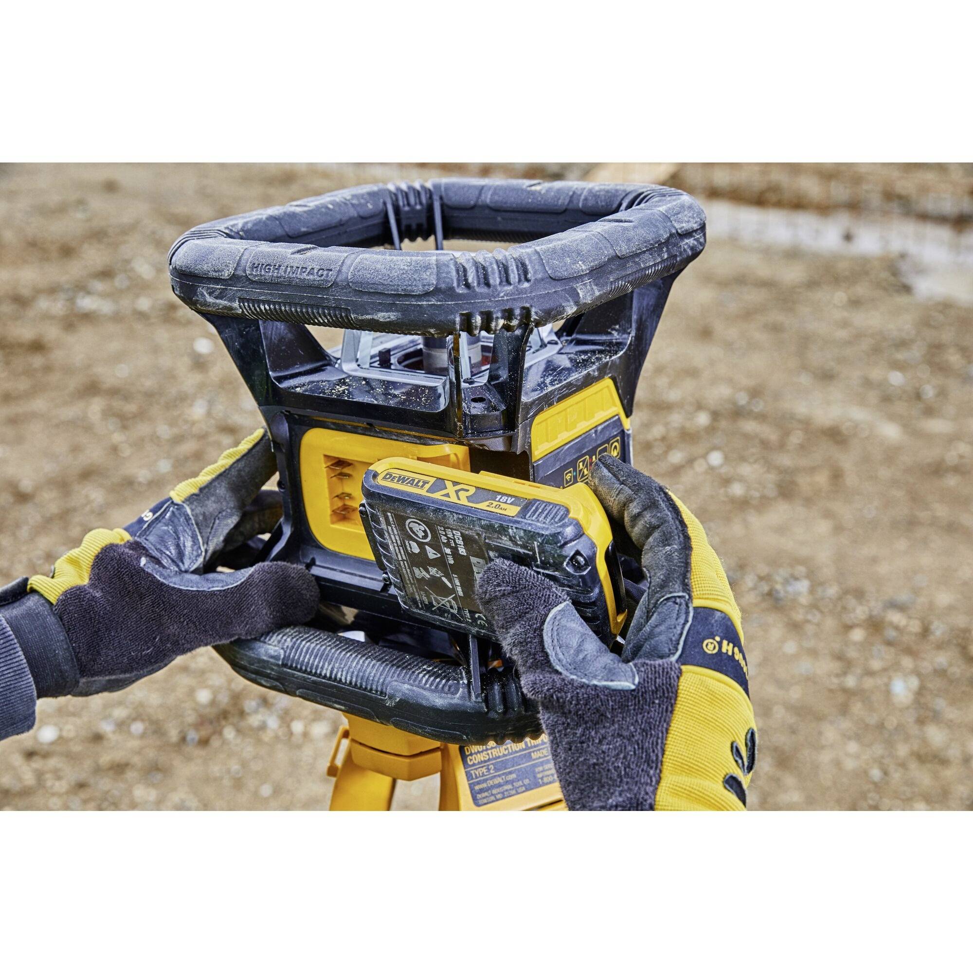 Eine Person mit gelben Handschuhen justiert ein Bau-Nivelliergerät auf einer Baustelle.