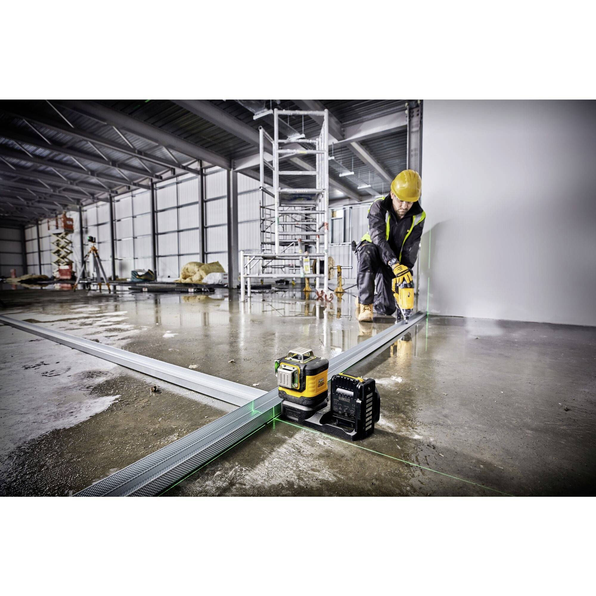 Eine Person in Arbeitskleidung und Schutzhelm verwendet in einer großen Halle einen Laser zur genauen Verlegung von Metallprofilen auf einem Betonboden.