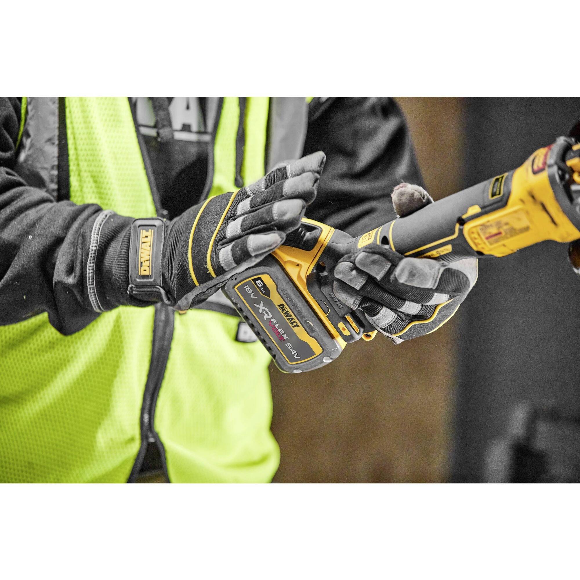Person hält ein gelbes Elektro-Werkzeug mit Handschuhen und Sicherheitsweste. Der Fokus liegt auf der Handhabung und dem Gerät.