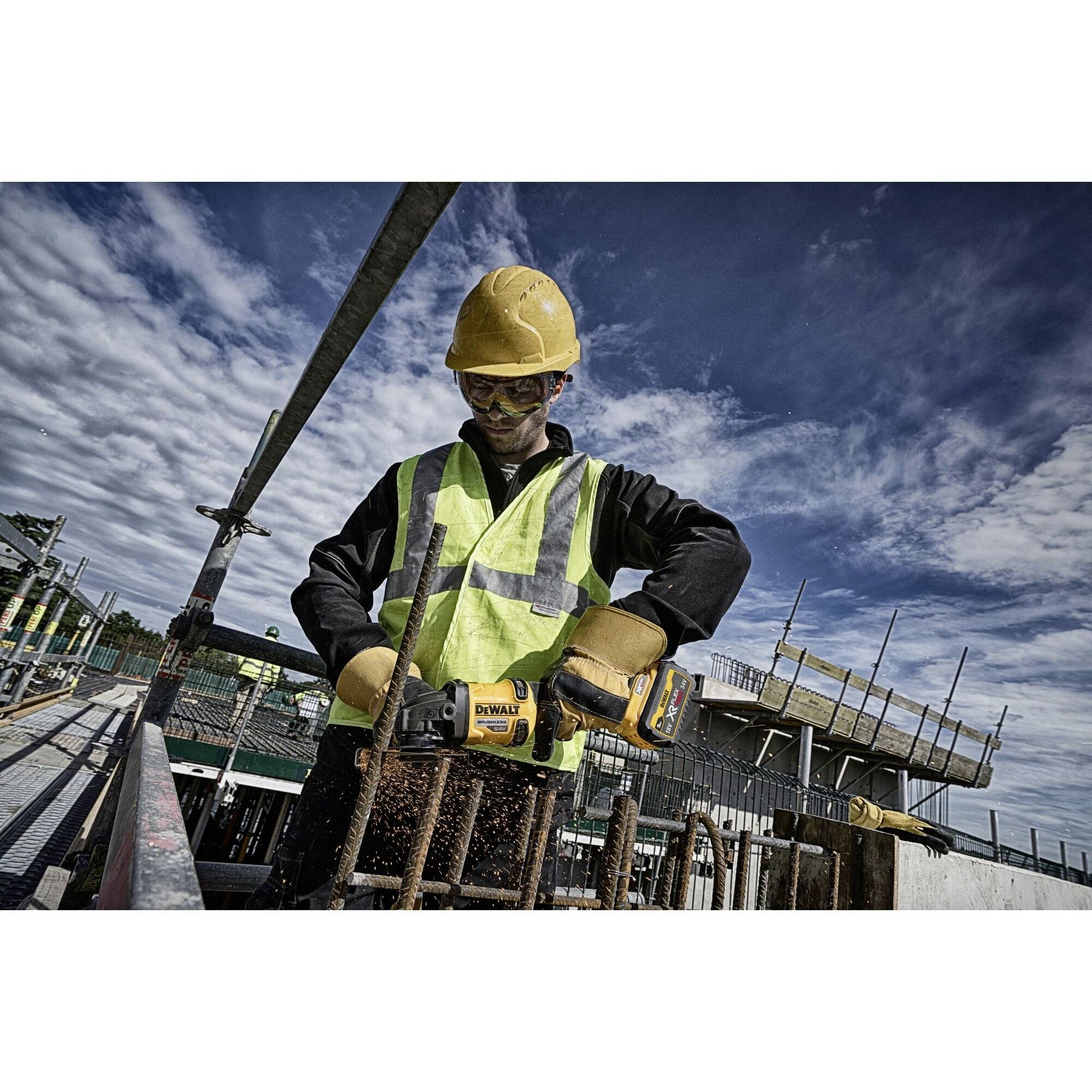 Ein Bauarbeiter mit Sicherheitsausrüstung schneidet Metallstäbe mit einer elektrischen Säge auf einer Baustelle unter blauem Himmel.