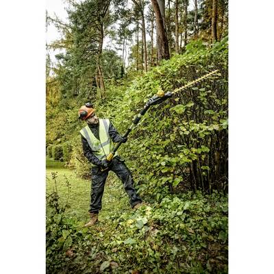 Ein Gärtner in Sicherheitskleidung schneidet mit einer langen Heckenschere eine Hecke im Wald.