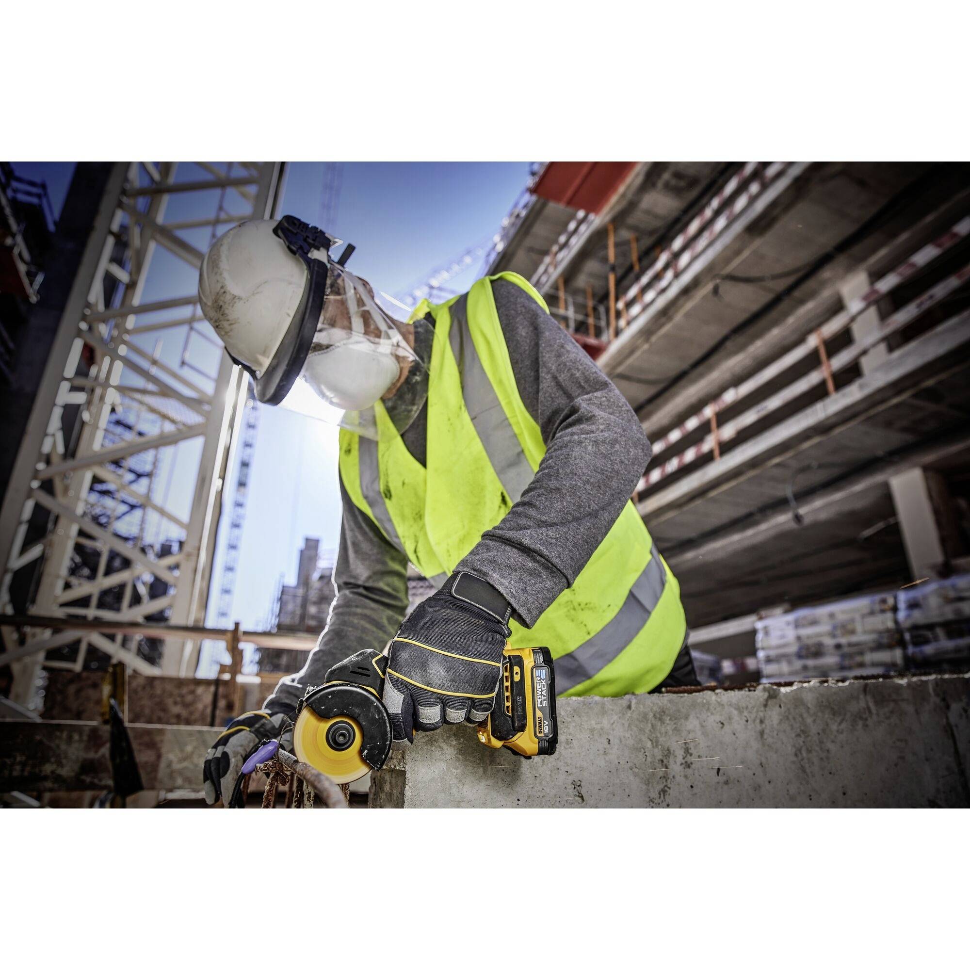 Ein Bauarbeiter in Schutzkleidung bedient eine Schleifmaschine auf einer Baustelle. Im Hintergrund sind Gerüste und Gebäude zu sehen.