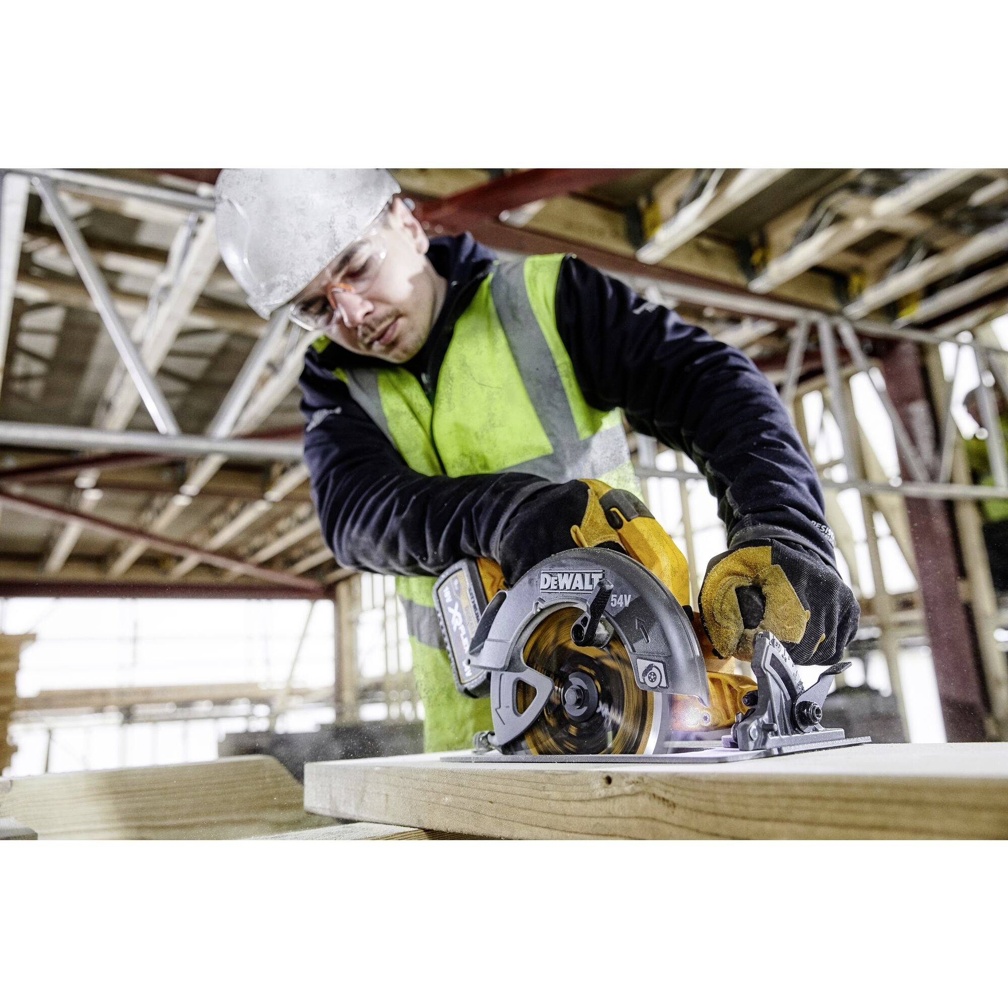 Ein Bauarbeiter mit Schutzkleidung schneidet mit einer Kreissäge Holz auf einer Baustelle. Im Hintergrund sind Gerüste sichtbar.