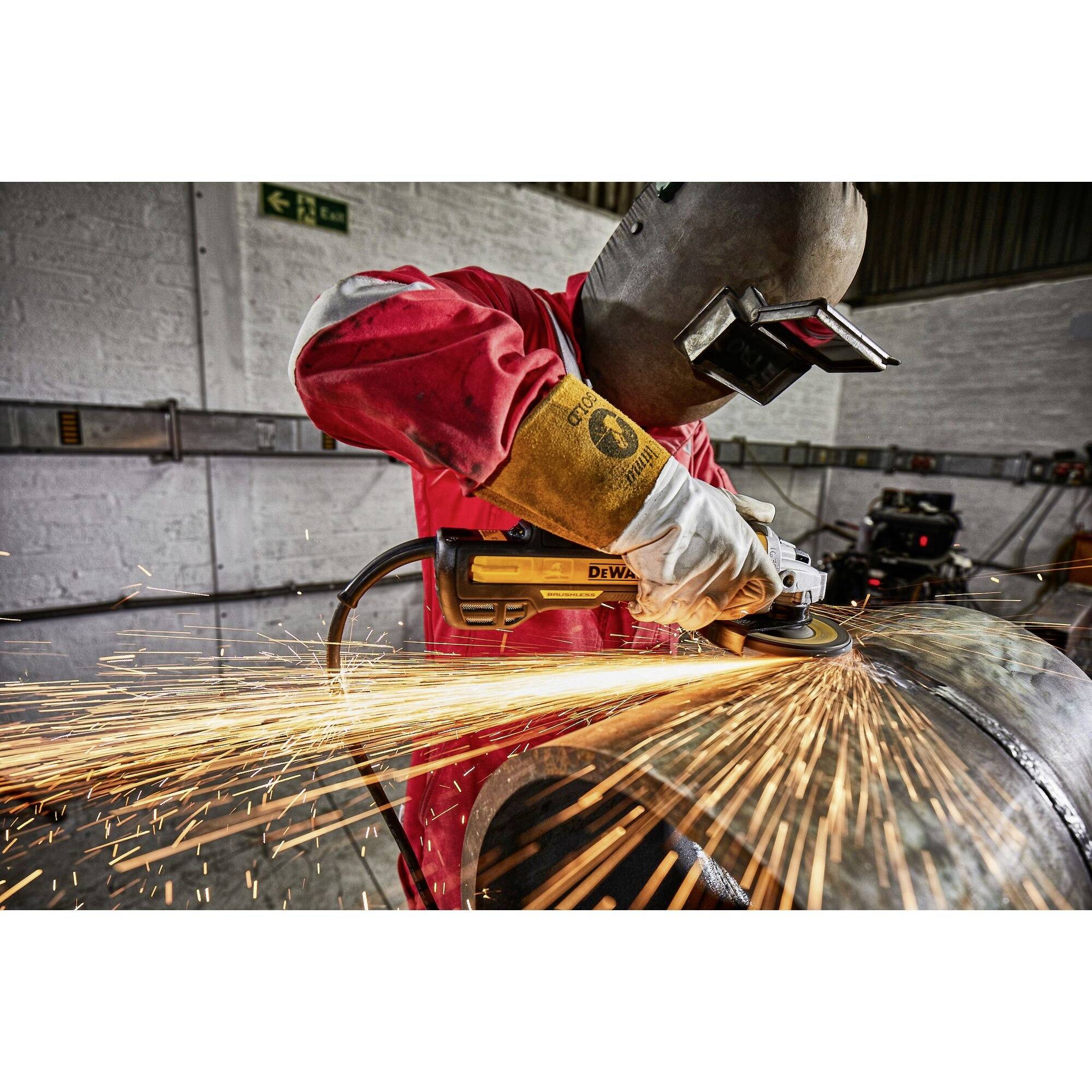 Ein Arbeiter mit Schutzhelm schleift ein Metallrohr. Funken sprühen, Sicherheitsausrüstung wird benutzt. Arbeitsumgebung in Werkstatt.