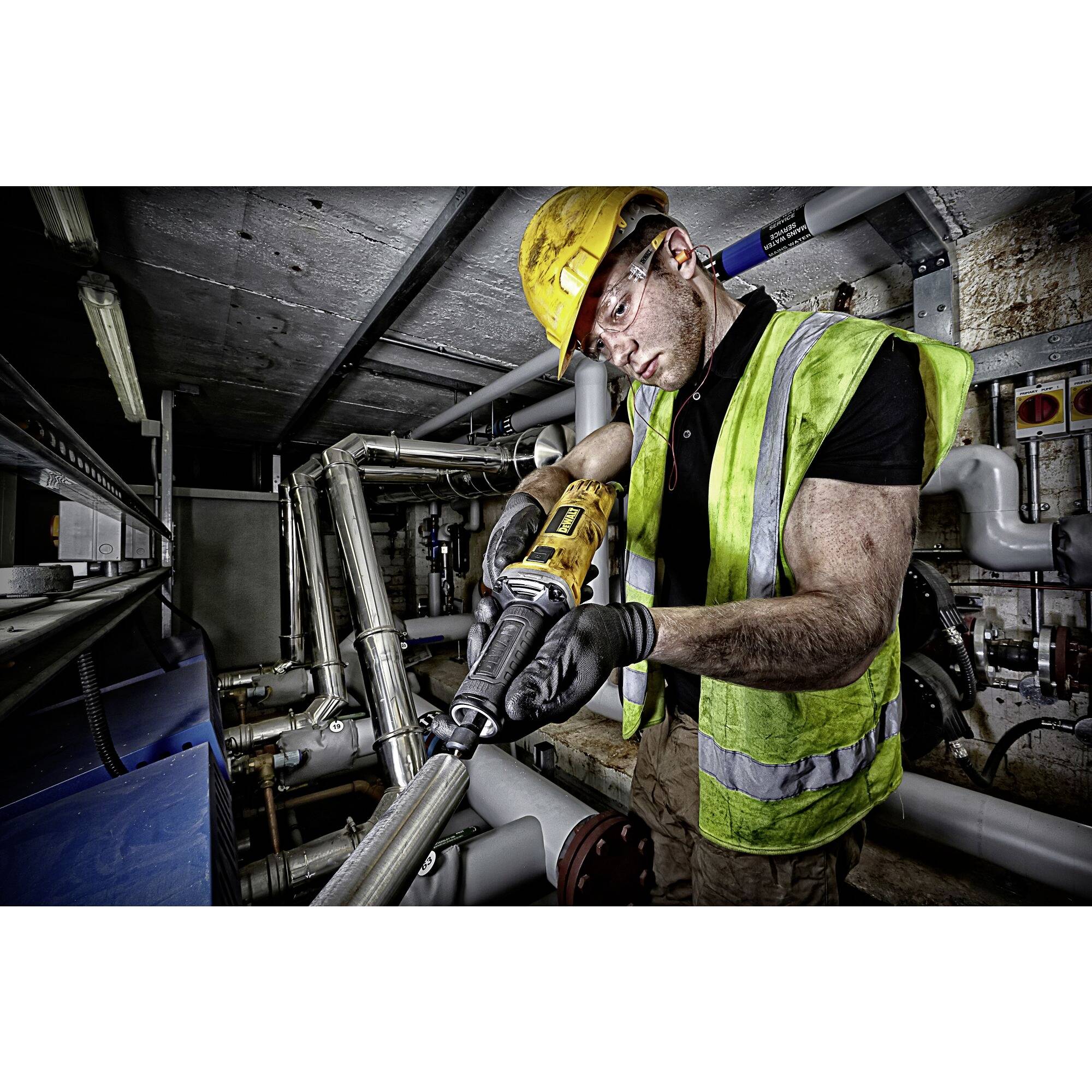 Ein Arbeiter mit gelbem Schutzhelm und Weste benutzt ein Elektrowerkzeug zur Rohrbearbeitung in einem industriellen Maschinenraum.