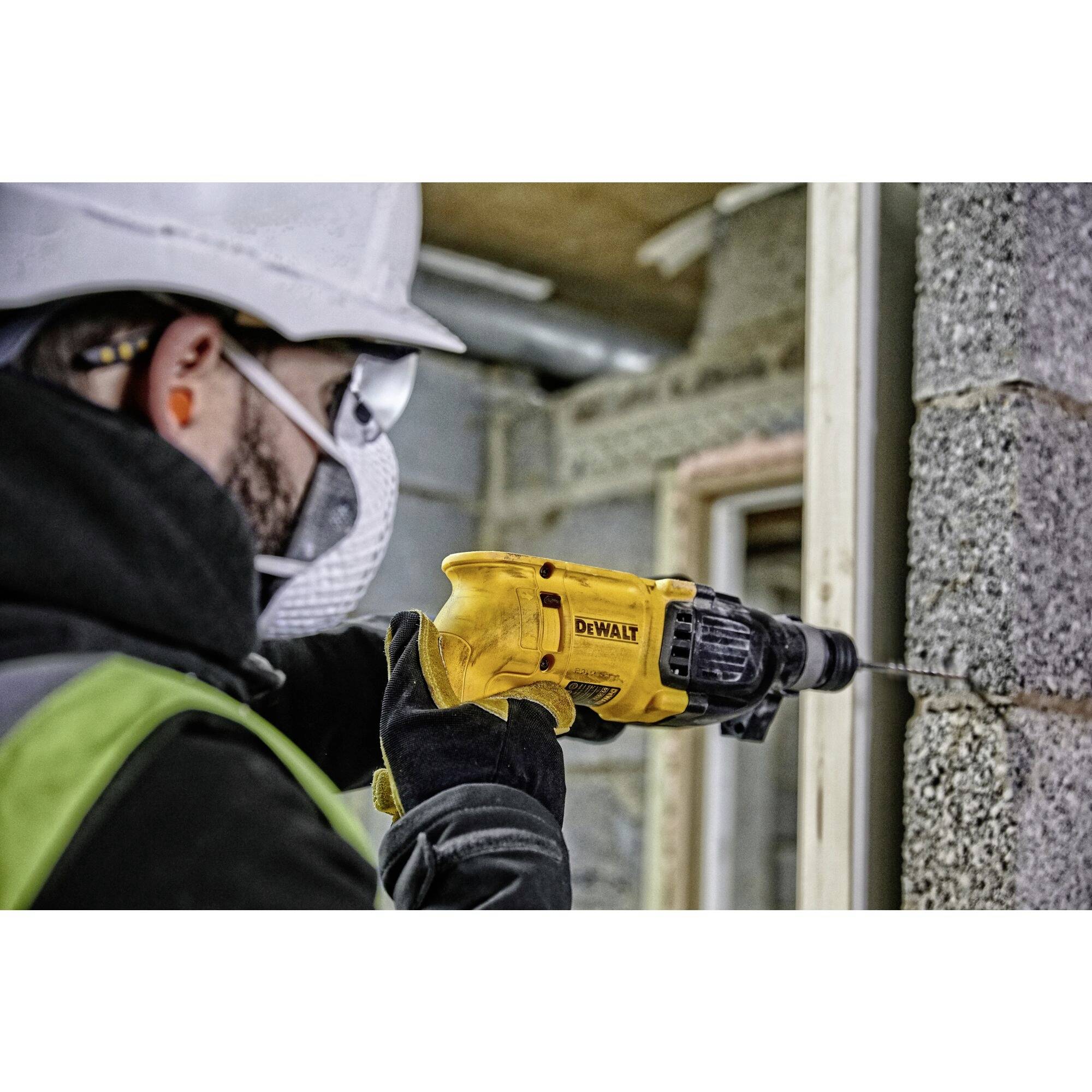 Eine Person bohrt mit einem gelben Elektrowerkzeug in eine Betonwand. Sie trägt Schutzkleidung, einschließlich Helm und Schutzbrille.