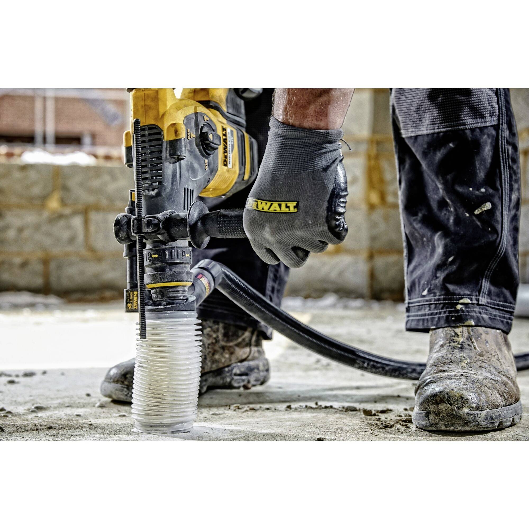 Ein Bauarbeiter benutzt einen gelben Bohrhammer auf einer Betonfläche. Im Hintergrund sind unscharfe, im Bau befindliche Mauern zu sehen.