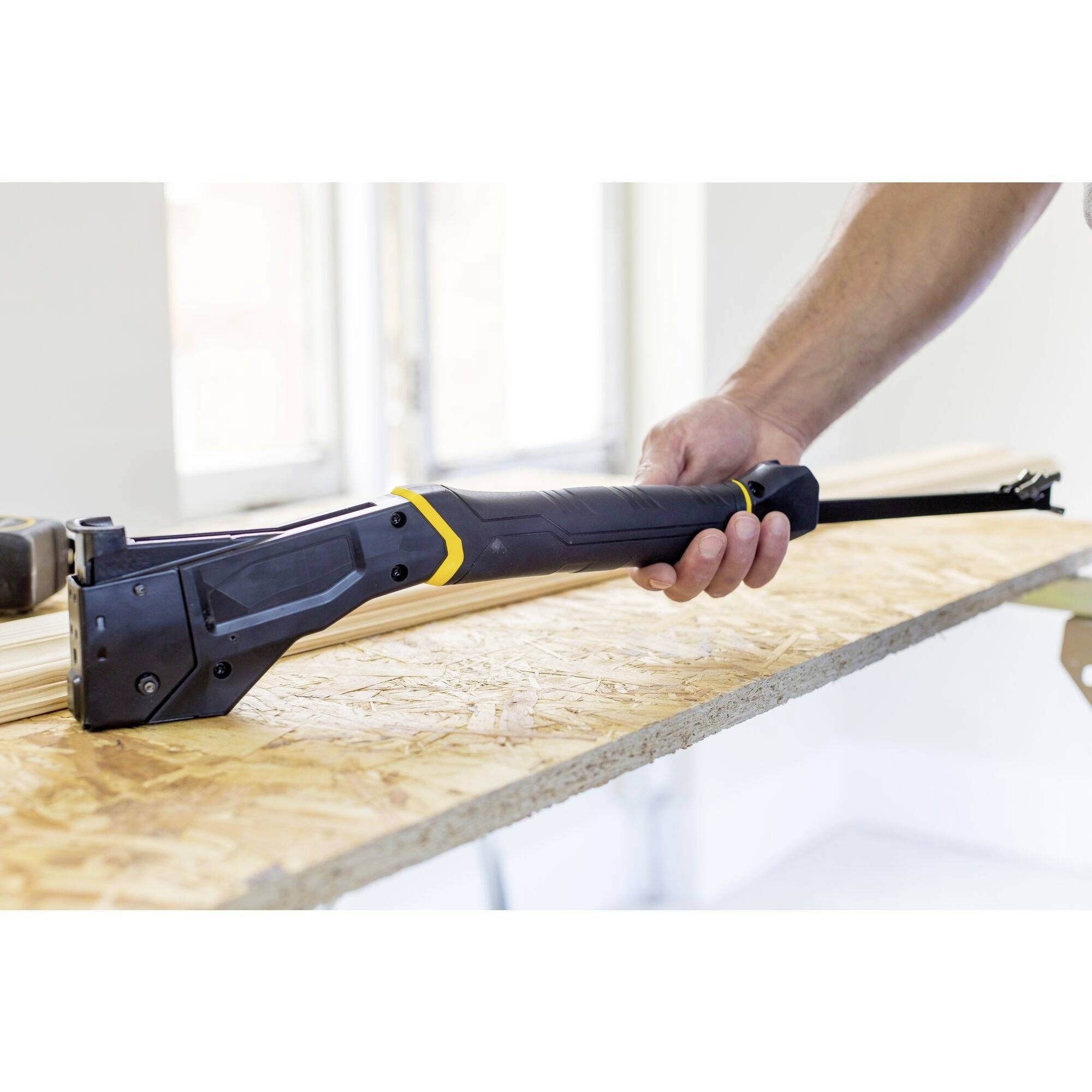 Eine Person sägt Holz mit einer tragbaren elektrischen Säge auf einer Tischplatte. Die Umgebung wirkt wie eine Werkstatt.