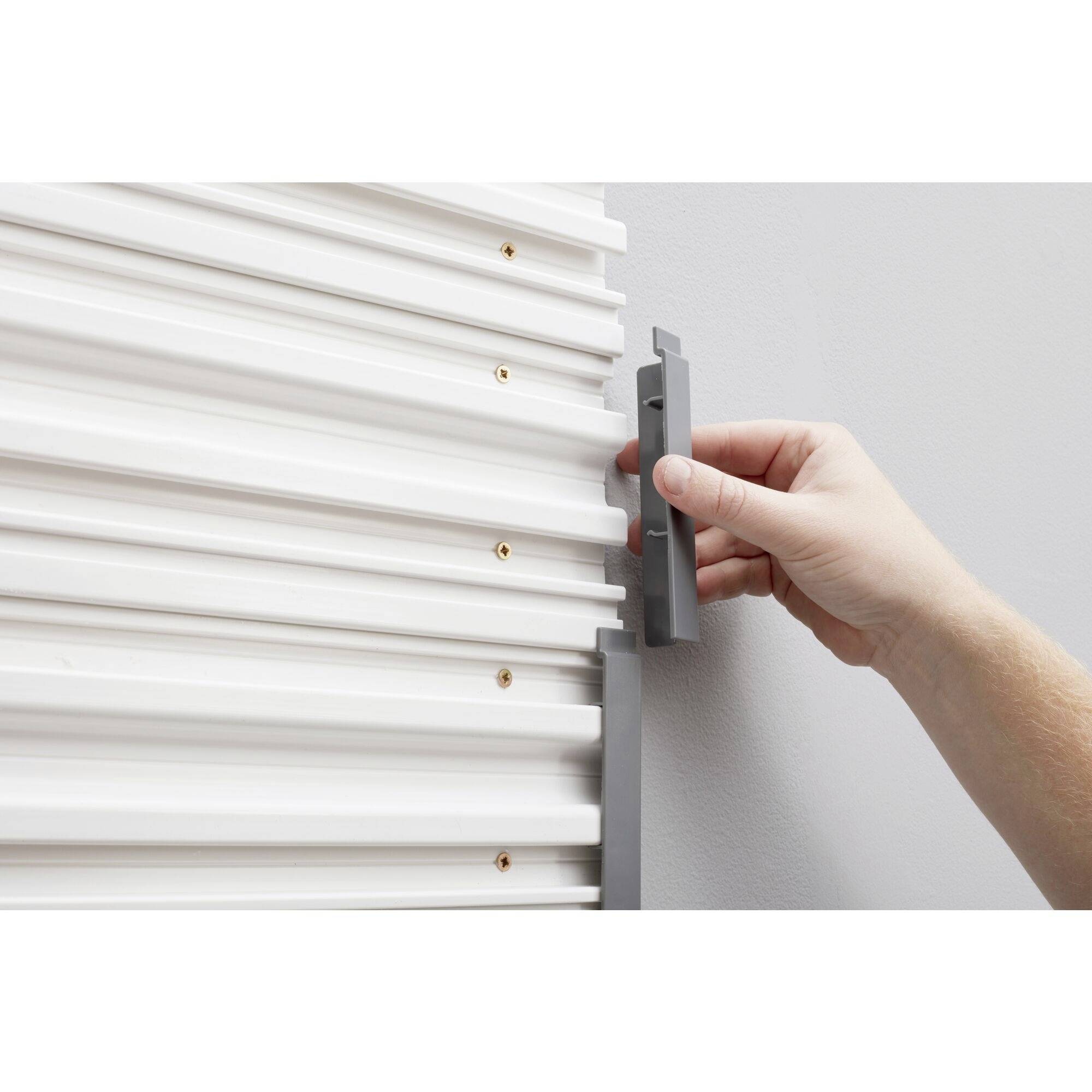 'Hand befestigt graue Halterung an weißem, strukturiertem Brett an der Wand.'