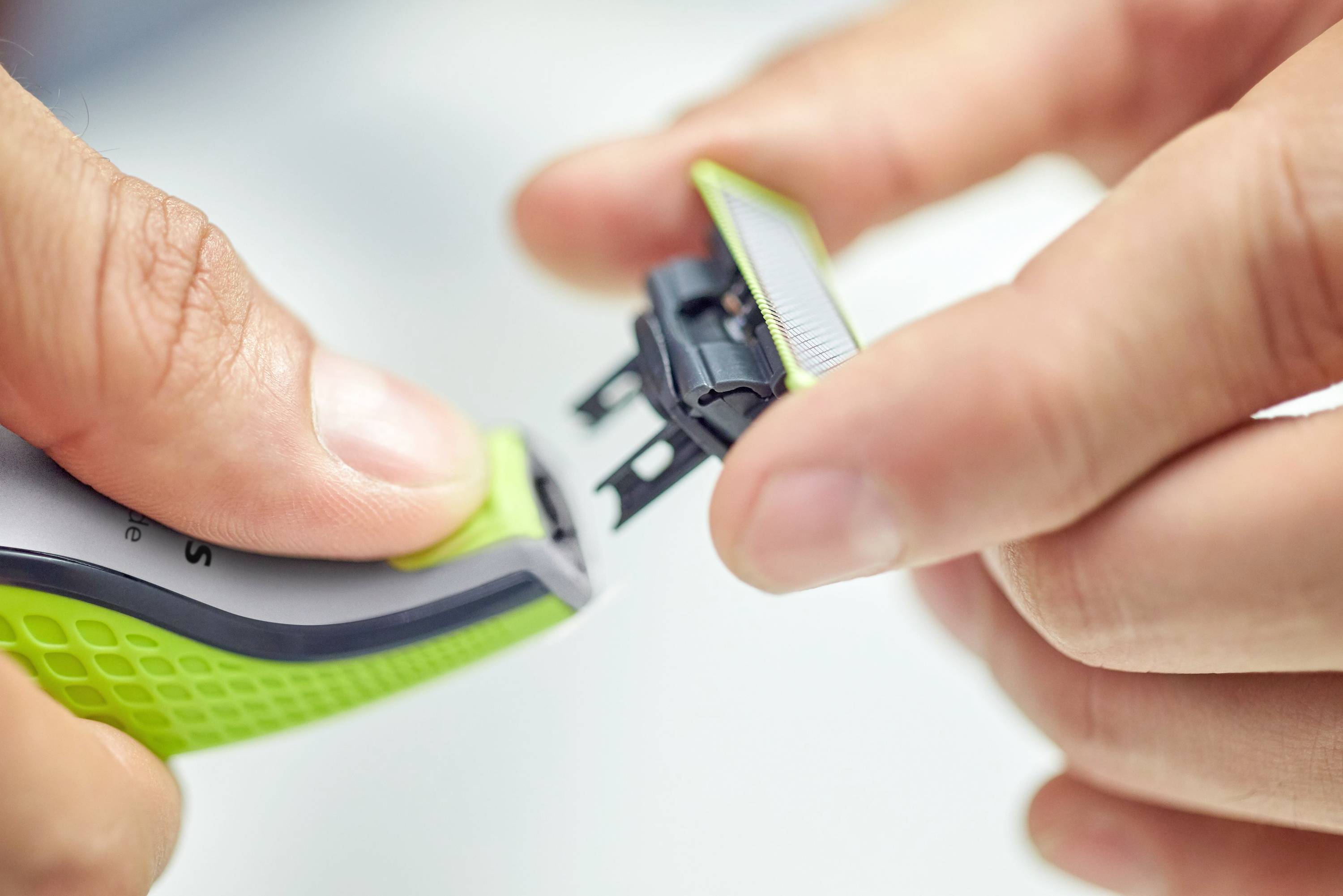Eine Person wechselst die Klinge eines elektrischen Rasierers, indem sie das Klingenteil abnimmt.