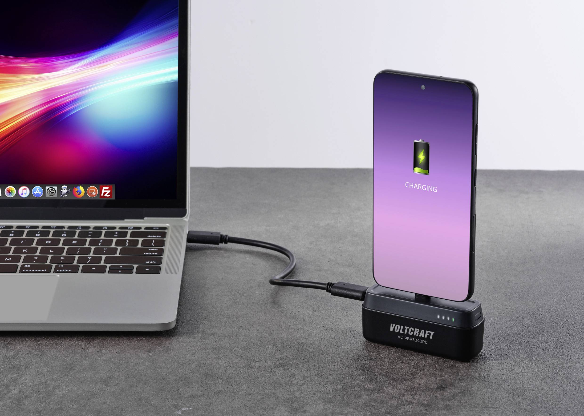 Ein Smartphone wird mit einem Kabel von einem Laptop aufgeladen. Der Bildschirm des Smartphones zeigt ein Ladesymbol.