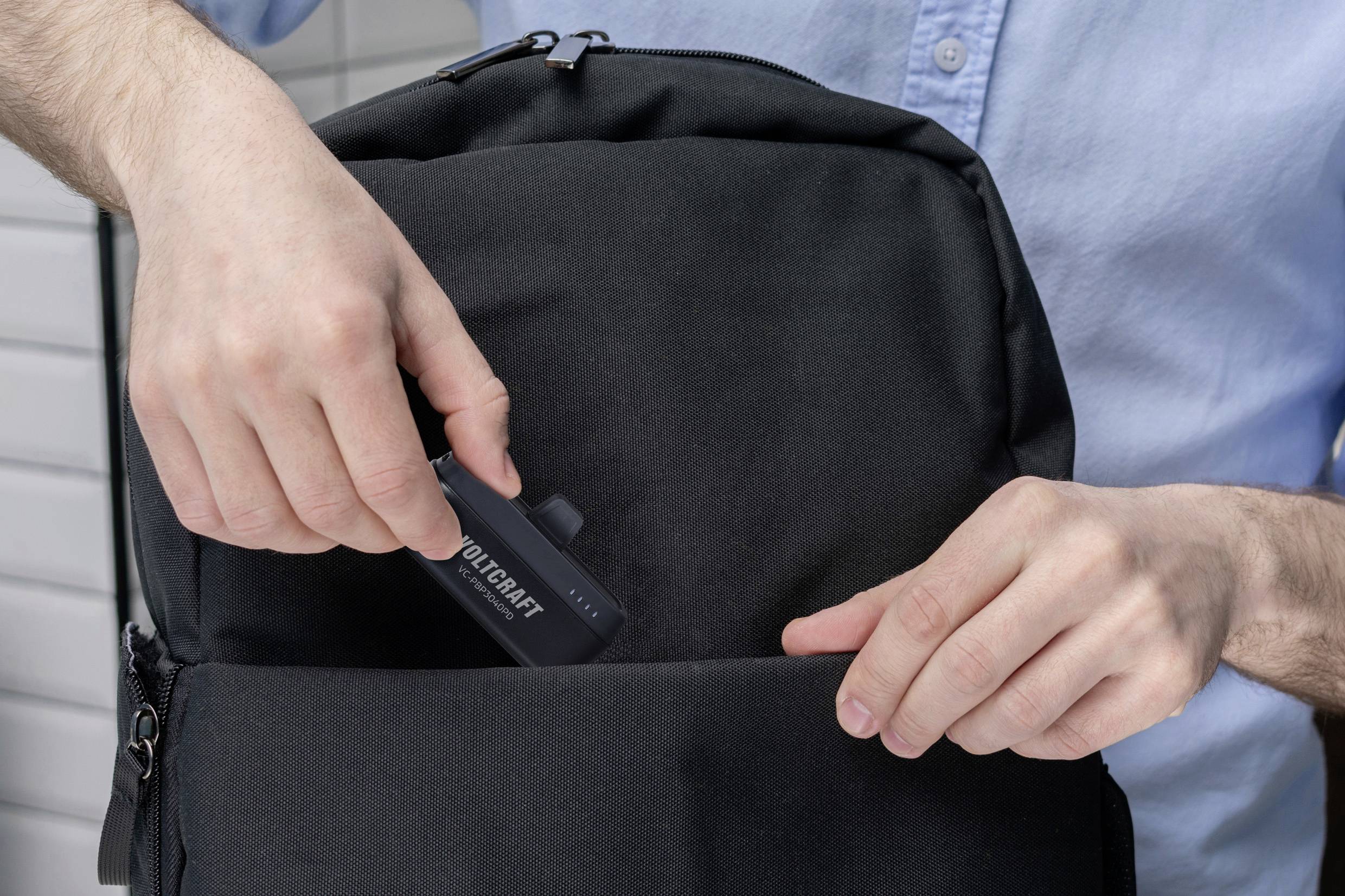 Person legt ein Werkzeugset in eine schwarze Rucksacktasche. Die Person trägt ein hellblaues Hemd.