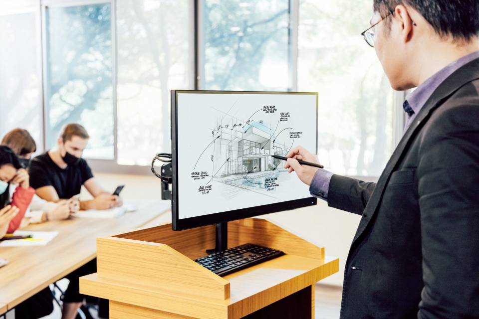Ein Mann präsentiert am Monitor einer Gruppe von Personen ein architektonisches Gebäude-Design in einem Büro oder Konferenzraum.