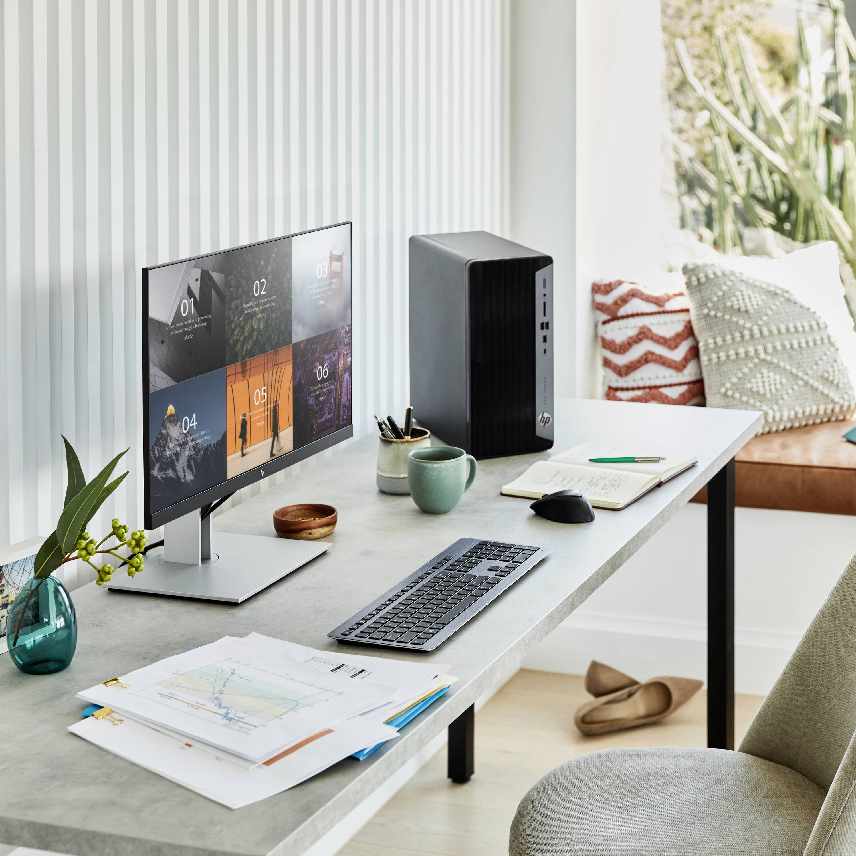 Ein moderner Schreibtisch mit Monitor, Tastatur, Maus und einem Desktop-PC. Daneben liegen Notizen, ein Stift und eine Pflanze.