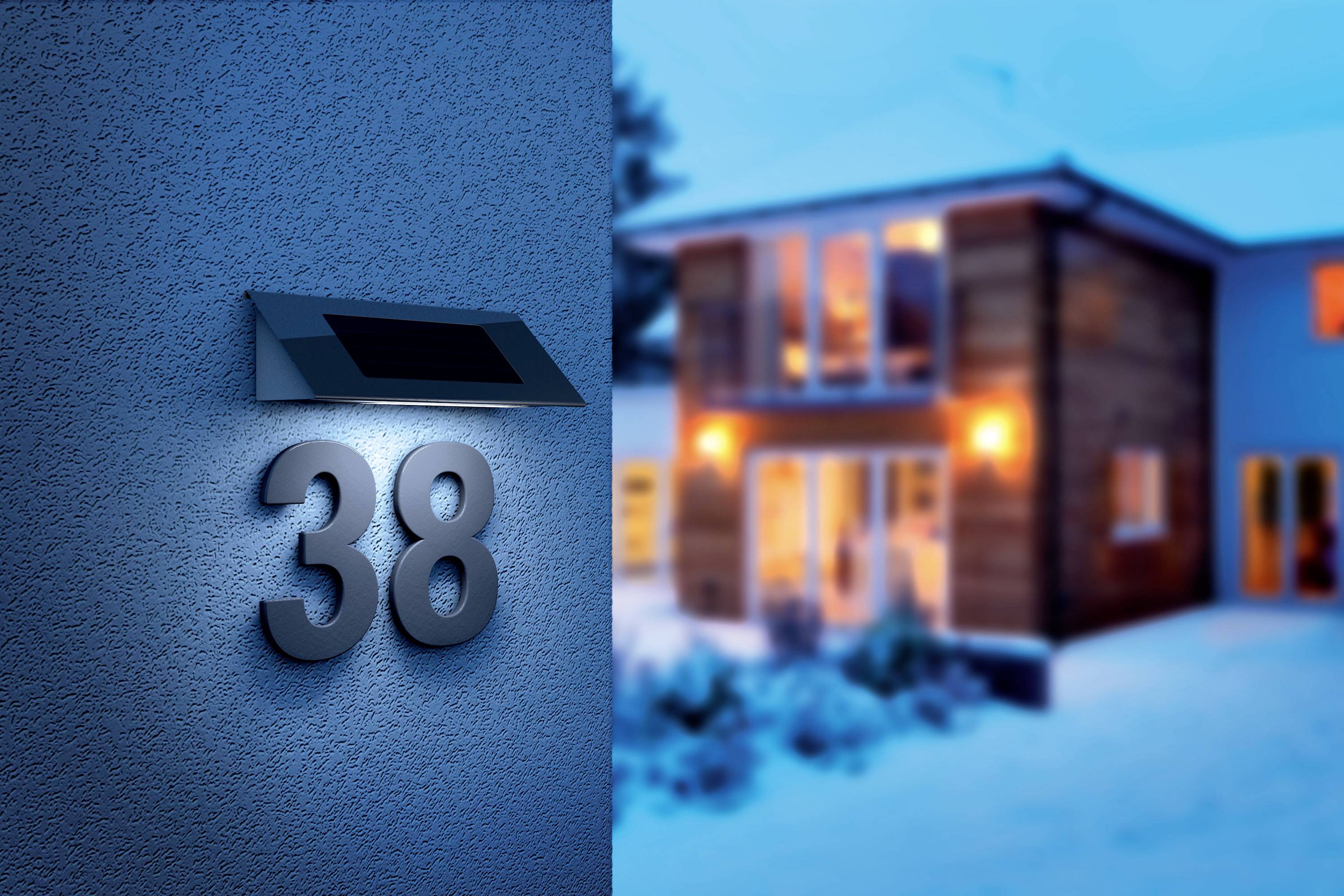 An einer Hauswand leuchtet die Nummer '38'. Im Hintergrund ist ein modernes Doppelhaus mit eingeschaltetem Licht zu sehen.