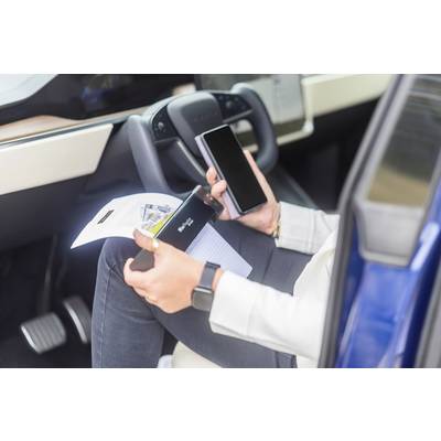 Person im Auto, hält Smartphone und Dokument. Lenkrad und Armaturenbrett im Hintergrund sichtbar. Moderne Technologie und Mobilität.