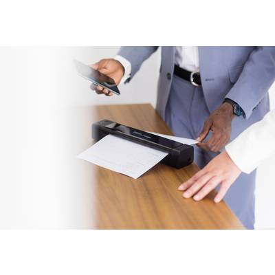 Zwei Personen scannen ein Dokument mit einem mobilen Scanner auf einem Holztisch. Eine Person hält ein Smartphone in der Hand.