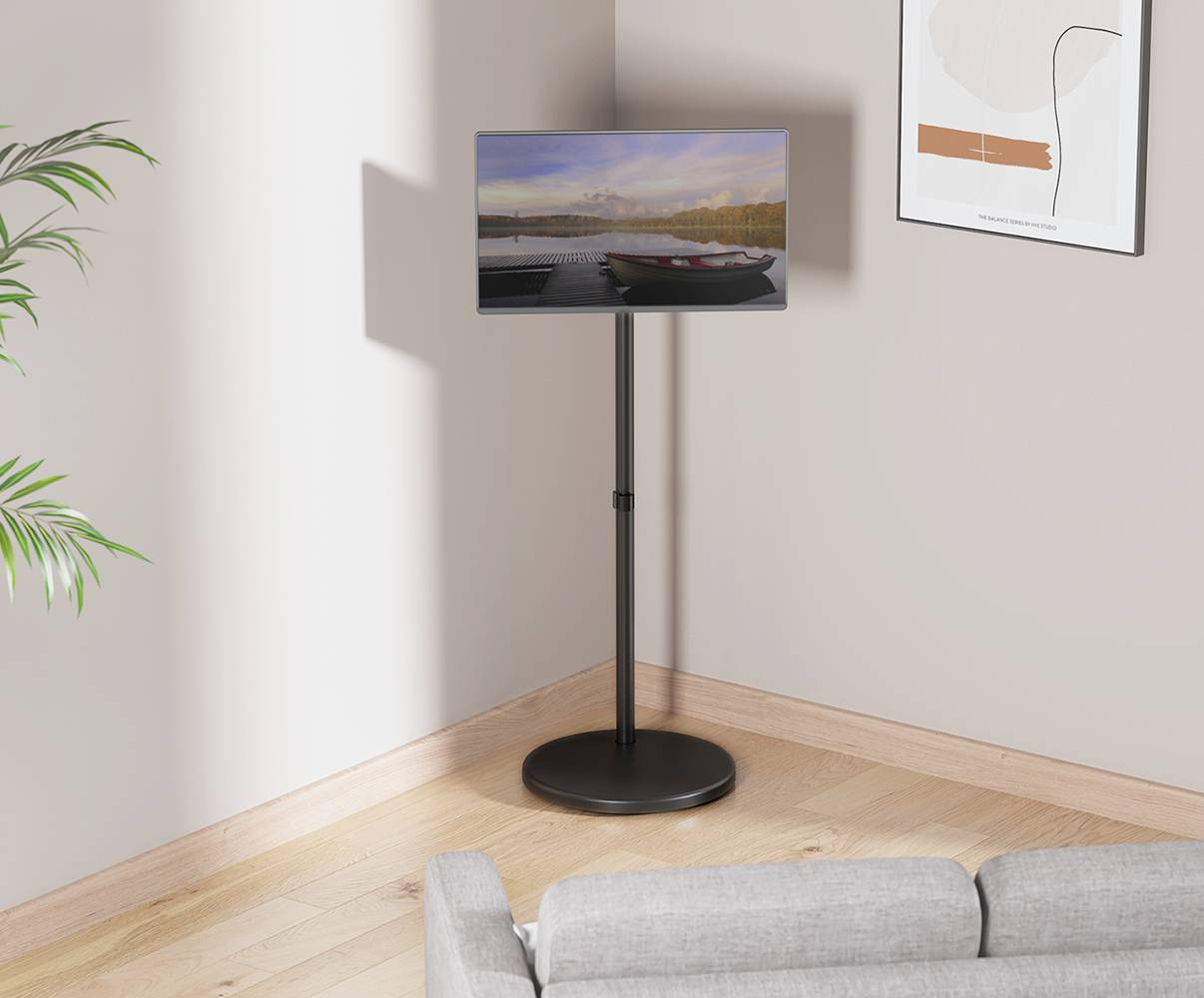 Ein Bildschirm auf einem schwarzen Ständer zeigt eine verschwommene Landschaft. Er steht in einer hellen Ecke mit einem Sofa und Pflanzen.