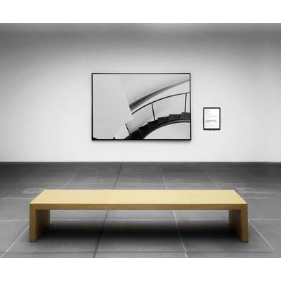 Ein minimalistischer Raum mit einem Holzbank in der Mitte vor einem modernen abstrakten Kunstwerk an der Wand.