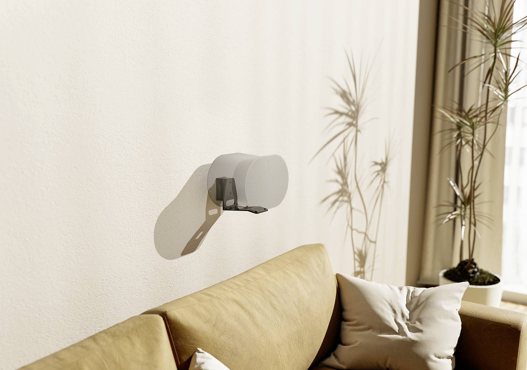 Lautsprecher an der Wand über einem beigen Sofa mit Kissen, im Hintergrund Pflanzen und ein Fenster mit Tageslicht.