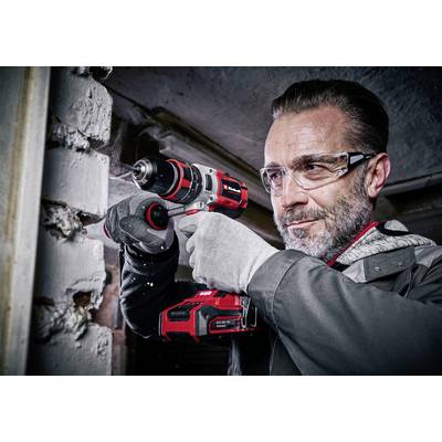 Ein Mann trägt Schutzbrille und Handschuhe, während er eine rote und schwarze Bohrmaschine zur Arbeit an einer weißen Ziegelwand verwendet.