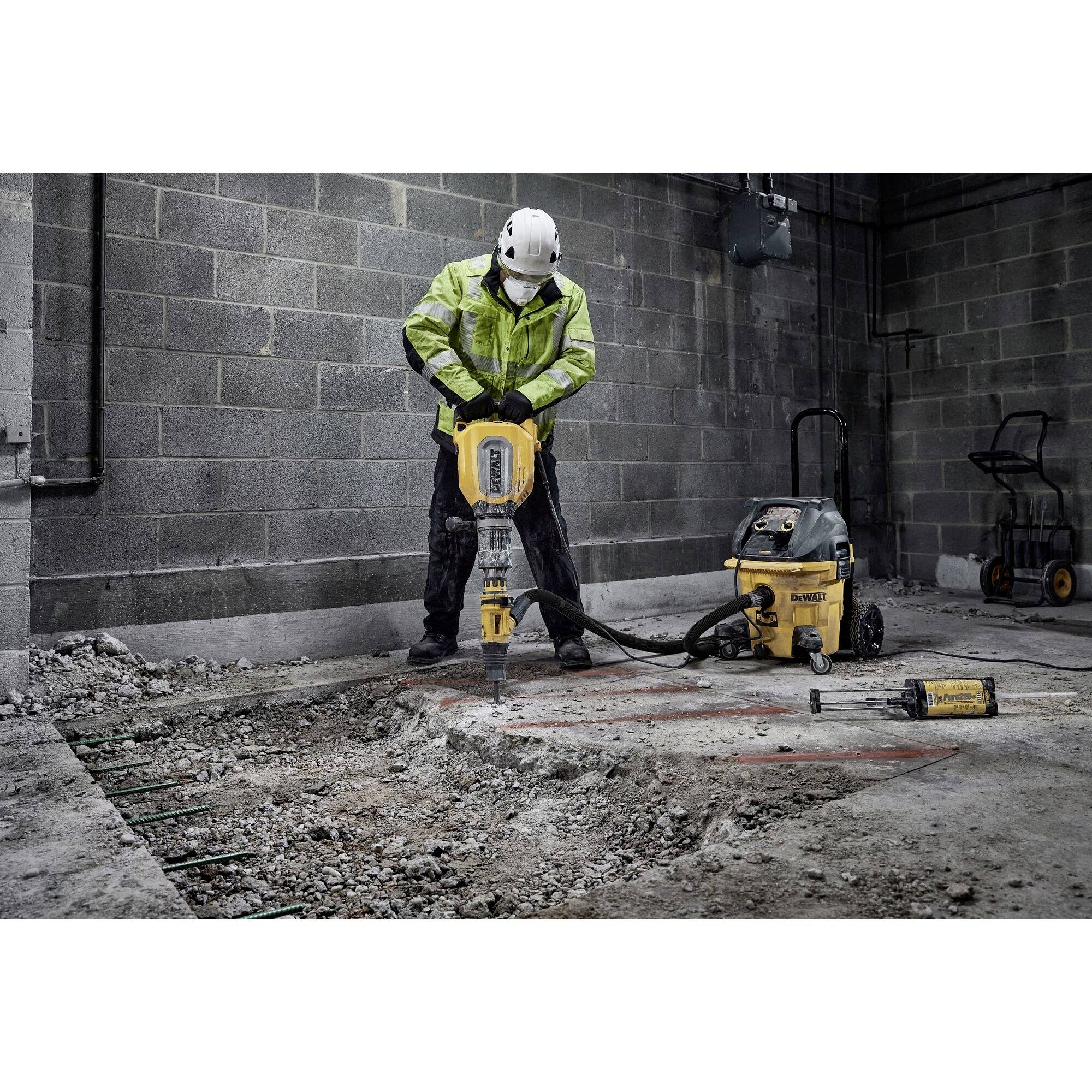 Eine Person in Schutzkleidung benutzt einen Abbruchhammer, um Beton in einer Baustellenumgebung zu durchbrechen.