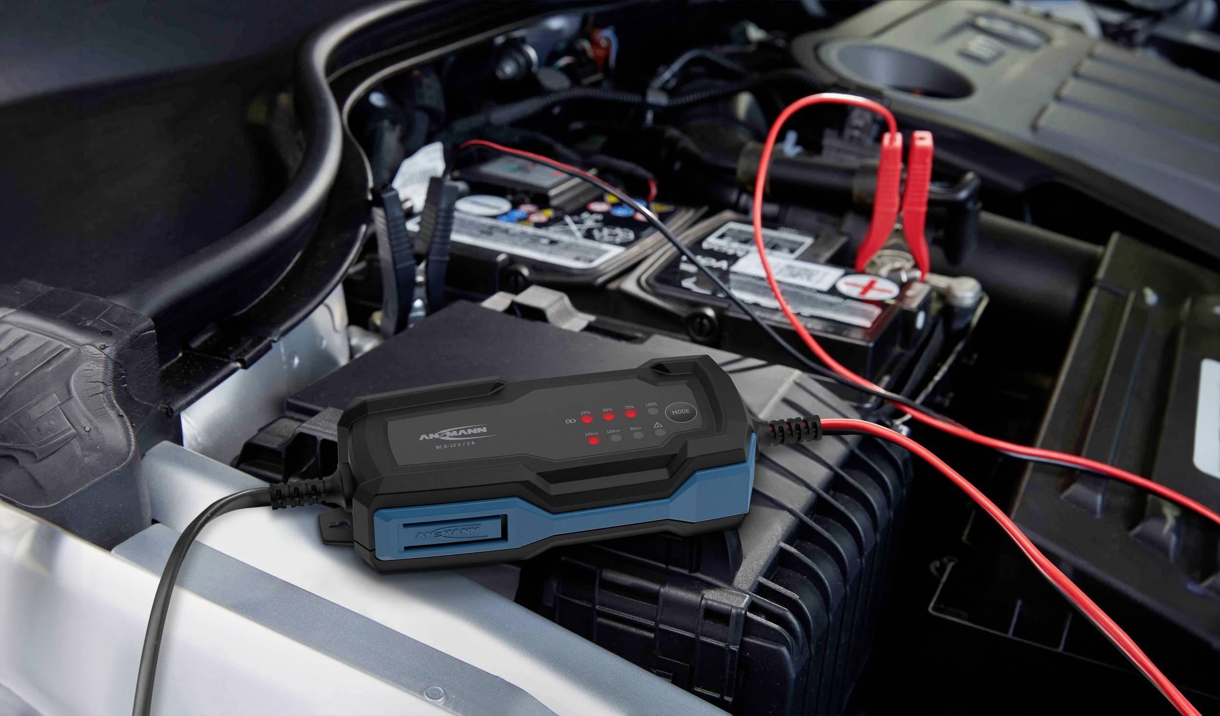 Ein Autobatterieladegerät ist an eine Autobatterie angeschlossen. Rote und schwarze Kabel verbinden das Gerät mit den Batterieklemmen.