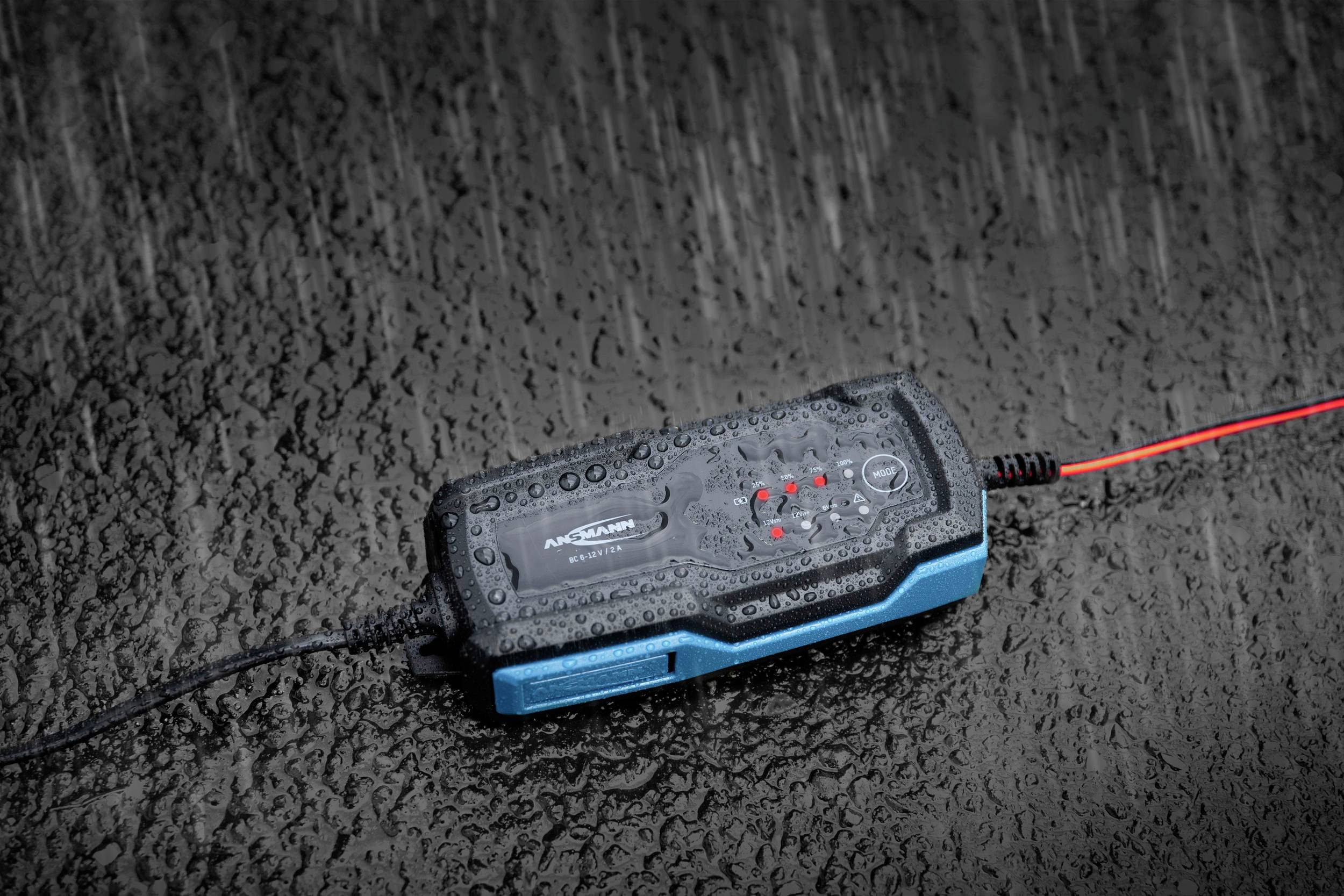 Ein batteriebetriebenes schwarzes und blaues Gerät mit leuchtenden roten LED-Anzeigen liegt auf nasser, regnerischer Oberfläche.