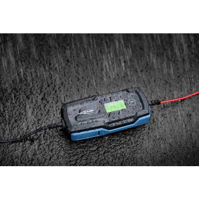 Ein Batterie-Ladegerät auf nasser Oberfläche im Regen, mit einem beleuchteten Display, das Informationen anzeigt.