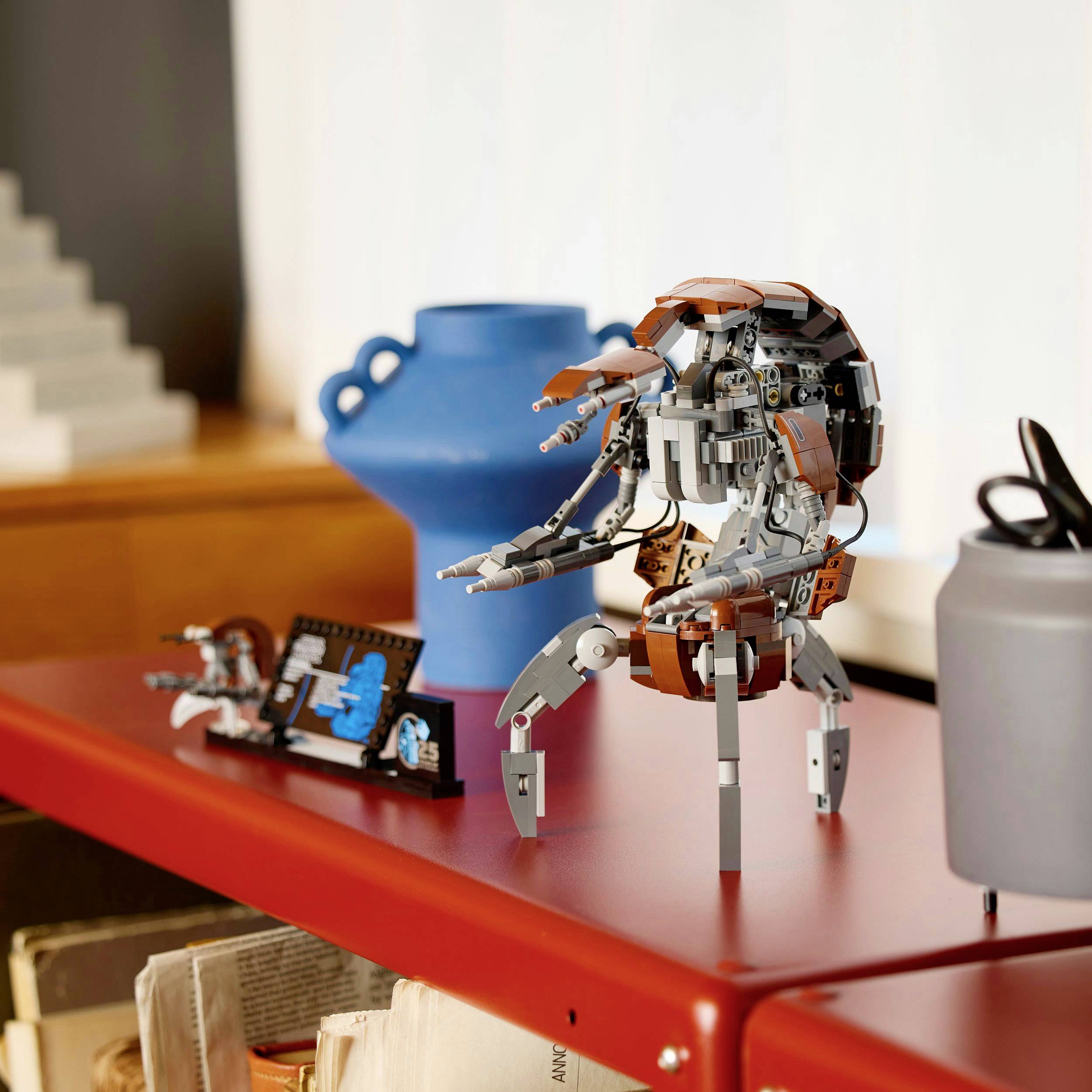 Ein Tisch mit Lego-Modellen: ein blauer Pokal, ein brauner Gecko-artiger Roboter mit langen Beinen, und kleine Figuren.