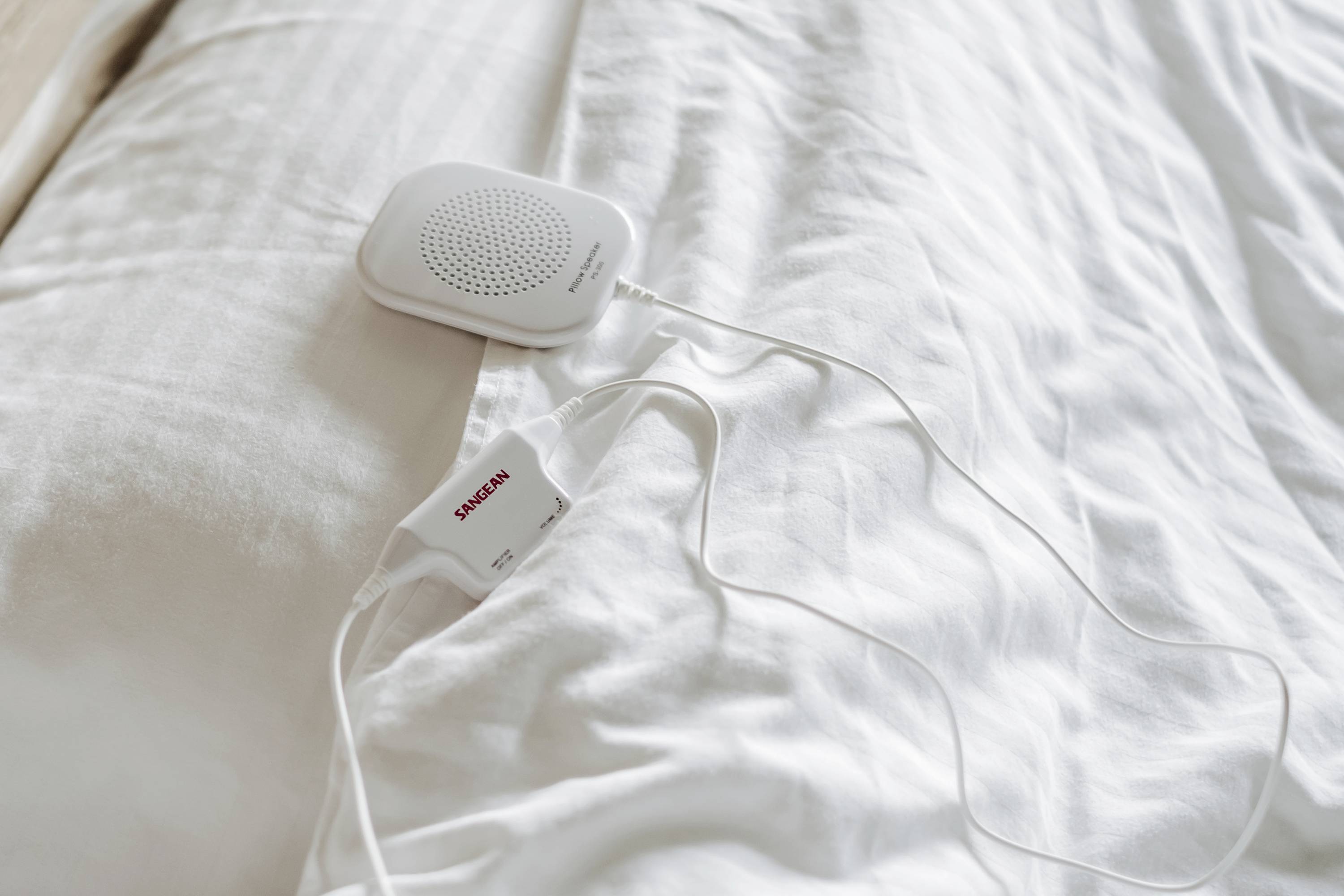 Ein weißer Lautsprecher mit Kabel liegt auf einem weißen Bettlaken. Ein Etikett mit der Aufschrift 'Samsung' ist sichtbar.