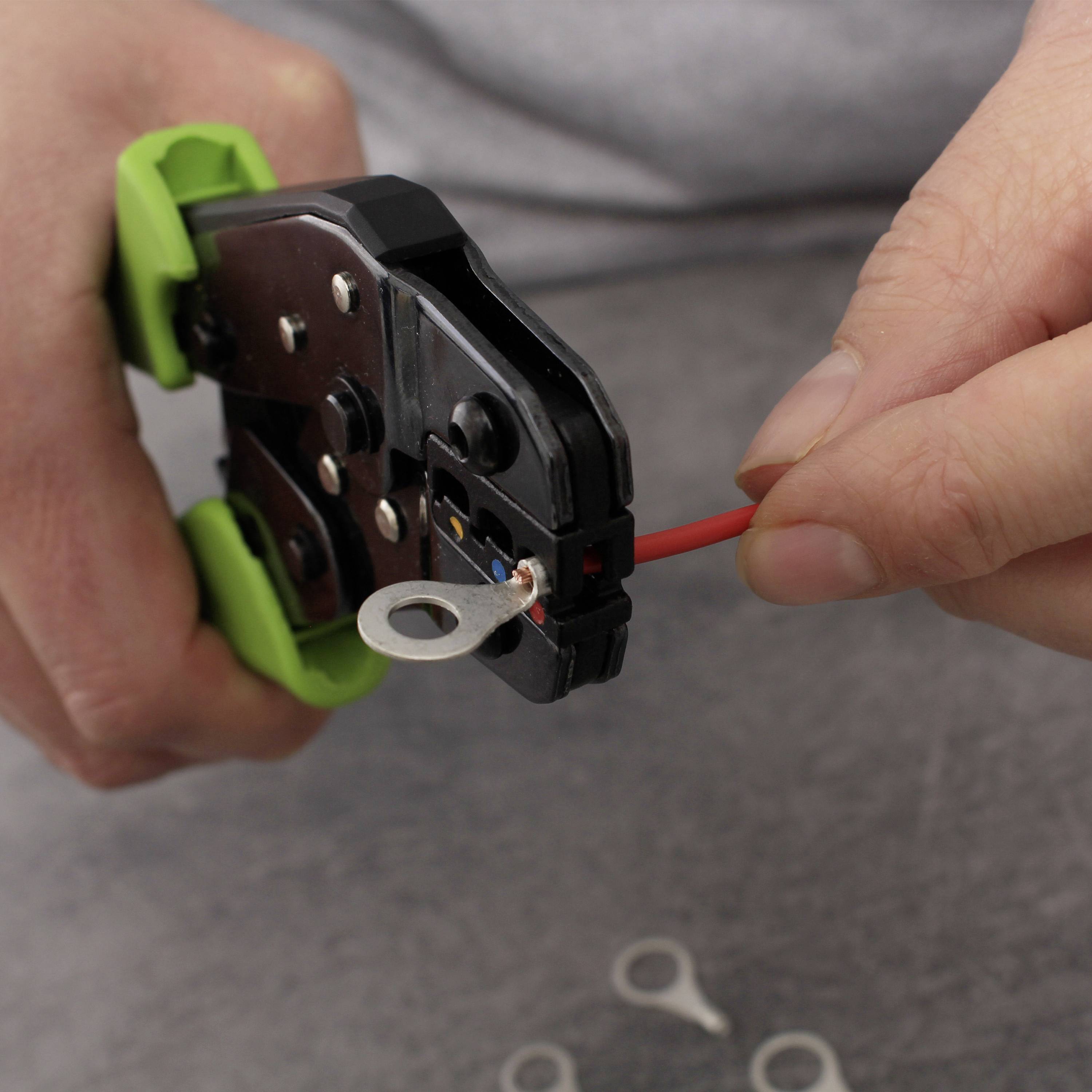 Person verwendet Crimpwerkzeug, um Kabel mit Kabelschuh zu verbinden. Nahaufnahme auf Tisch, konzentriert auf Handarbeit.