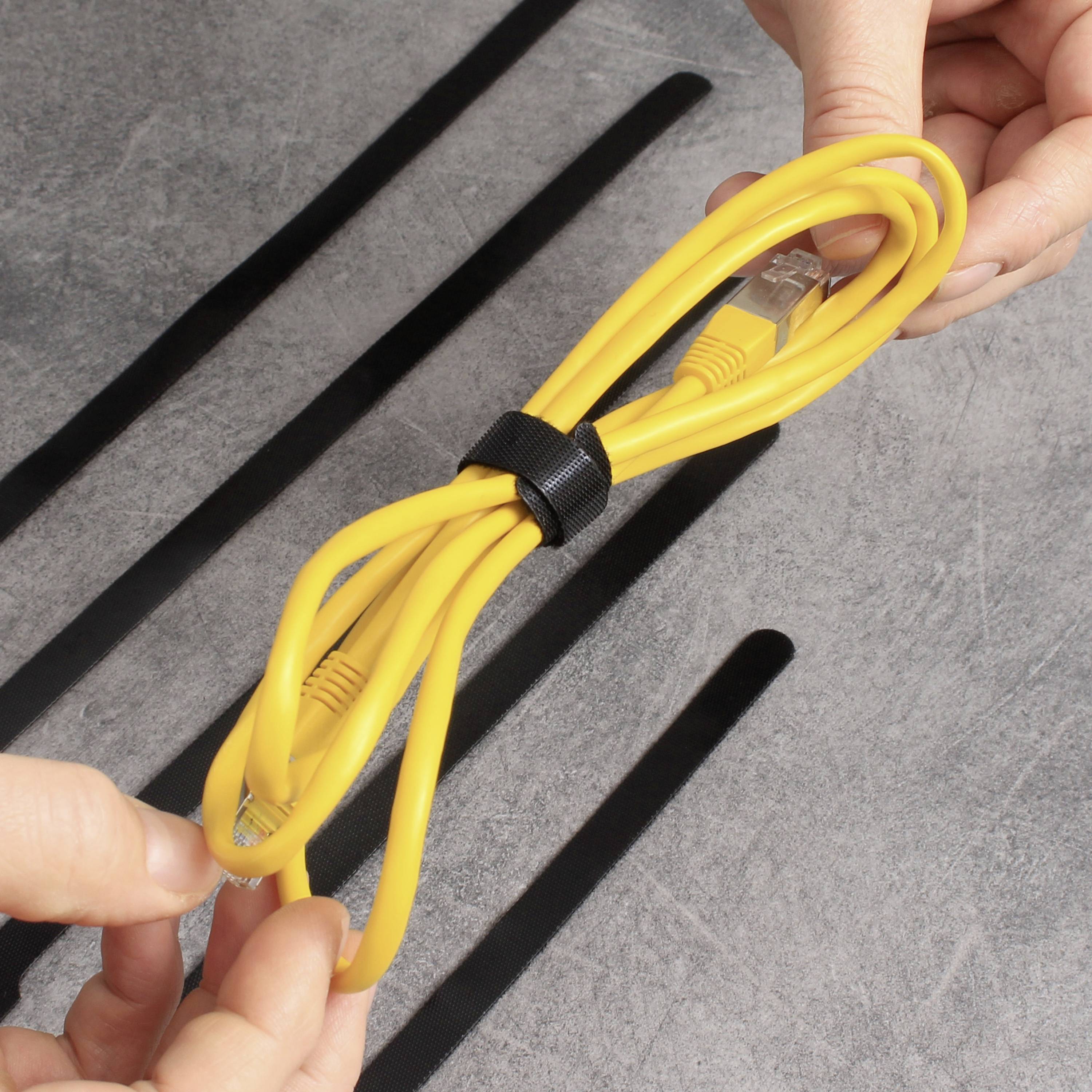 Eine Person hält ein gelbes Ethernet-Kabel, das mit einem schwarzen Klettverschluss zusammengebunden ist. Im Hintergrund sind schwarzfarbene Kabelkanäle auf einem grauen Tisch zu sehen.