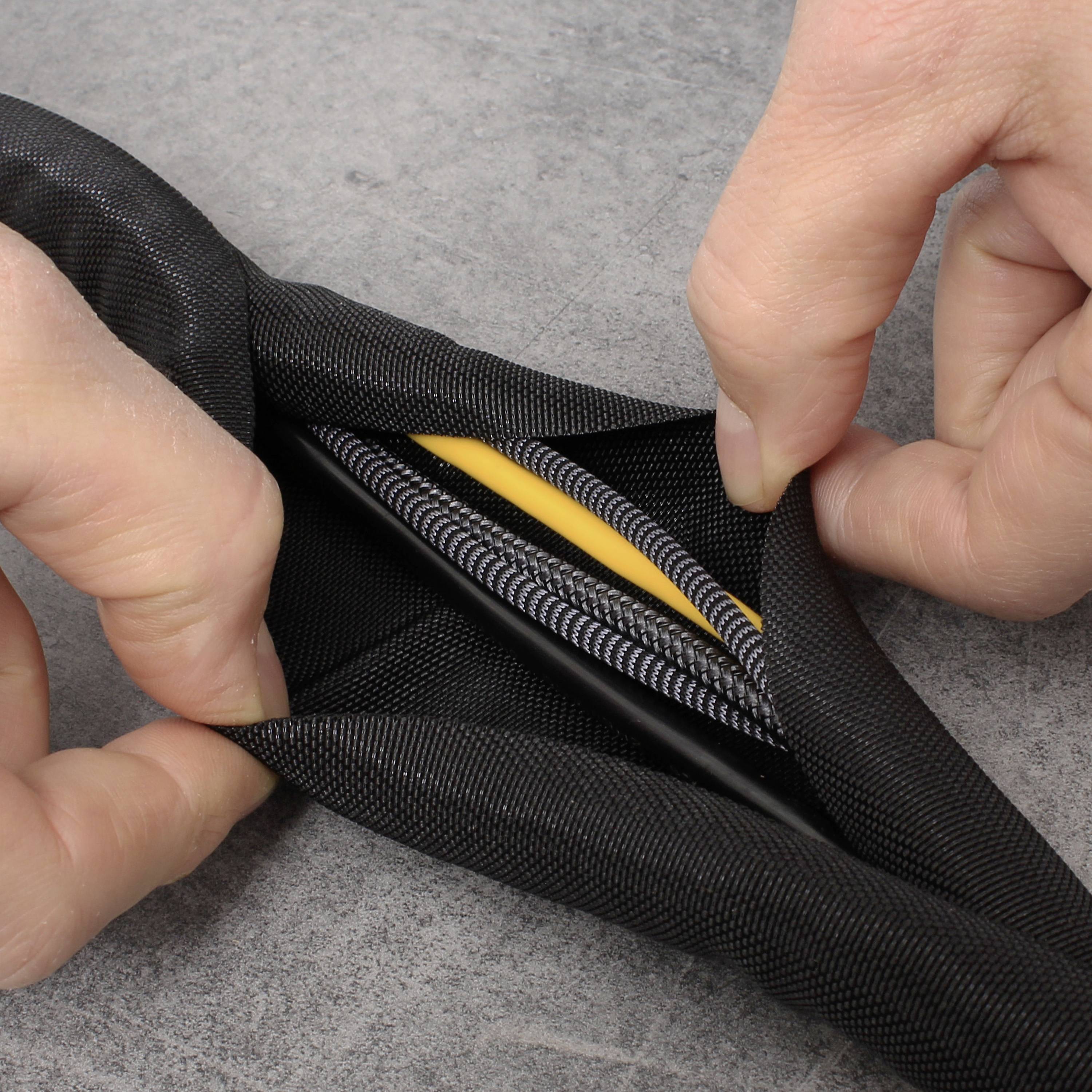 Hände halten ein flexibles Kabelschutzrohr, aus dem mehrere Kabel herausragen. Das Rohr ist schwarz, die Kabel sind schwarz und gelb.