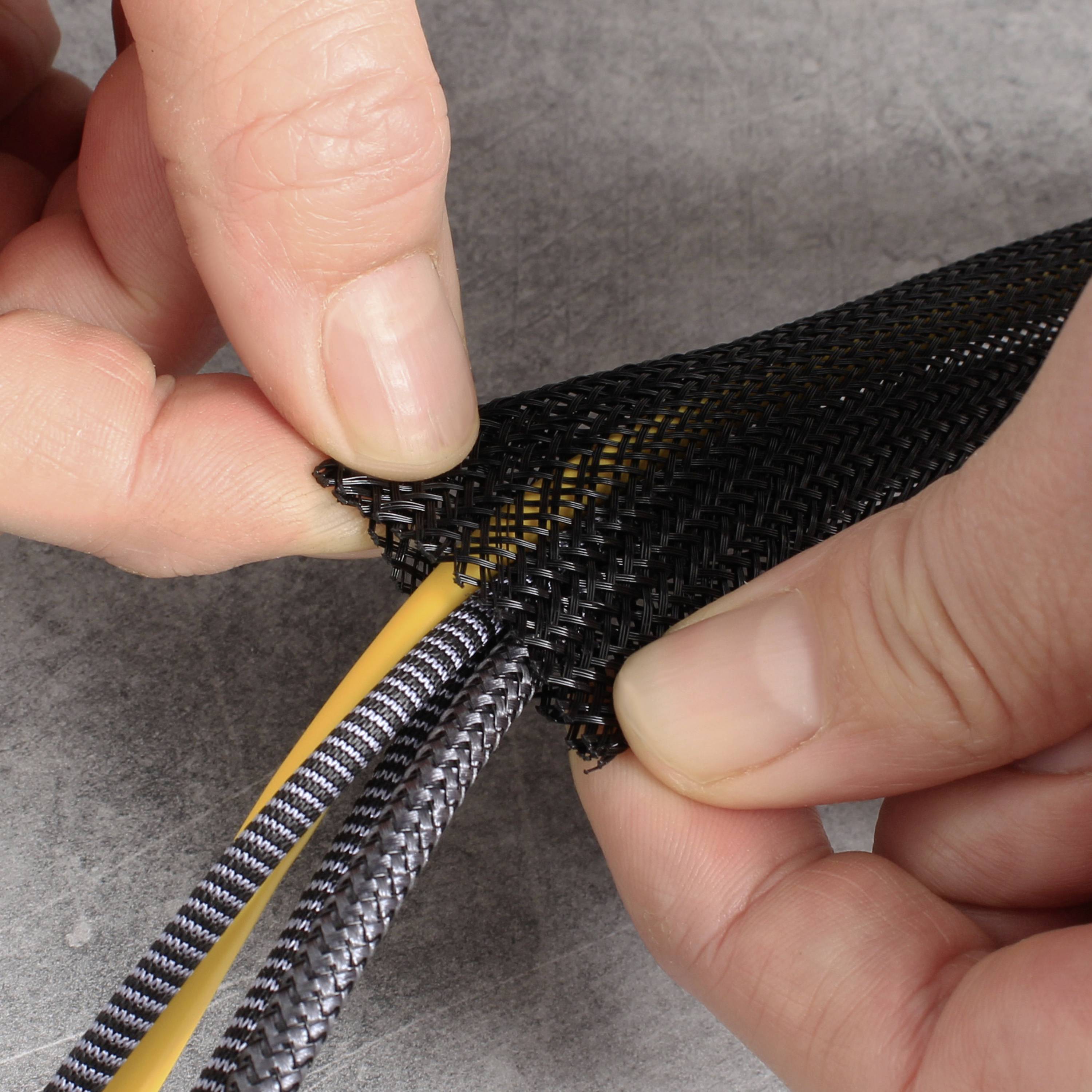 Zwei Hände zeigen ein schwarzes, geflochtenes Kabelmanagementrohr, das ein gelbes Kabel umschließt und schützt.