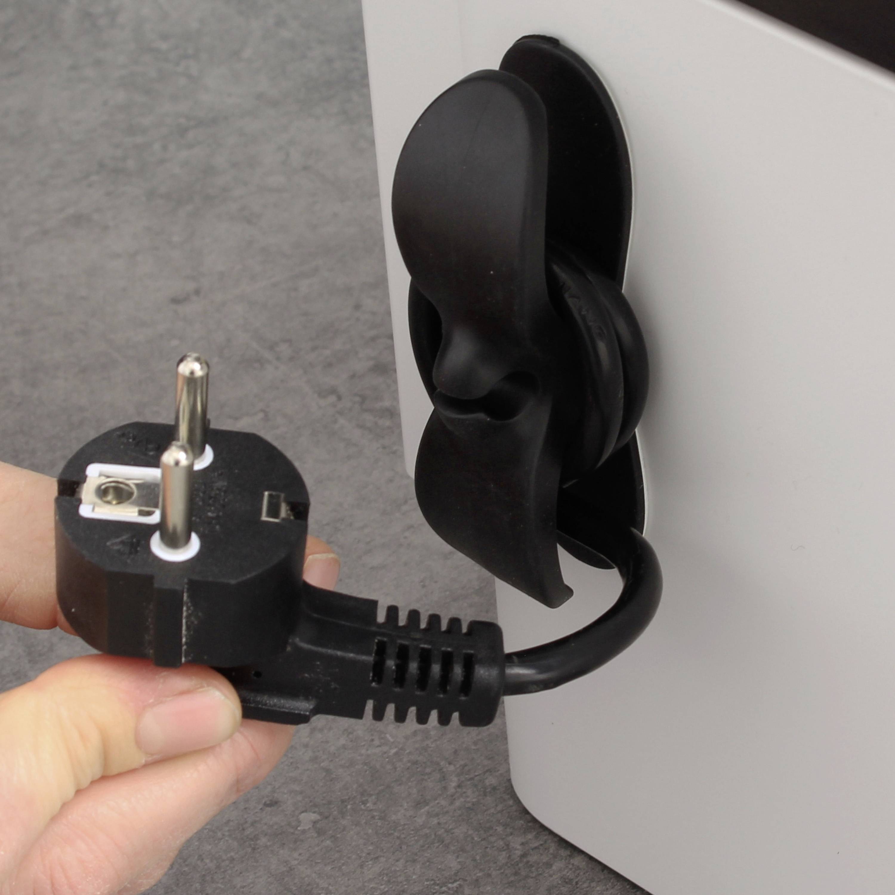 Eine Hand hält einen Stromstecker, der mit einem schwarzen Kabelhalter an der Wand befestigt ist.