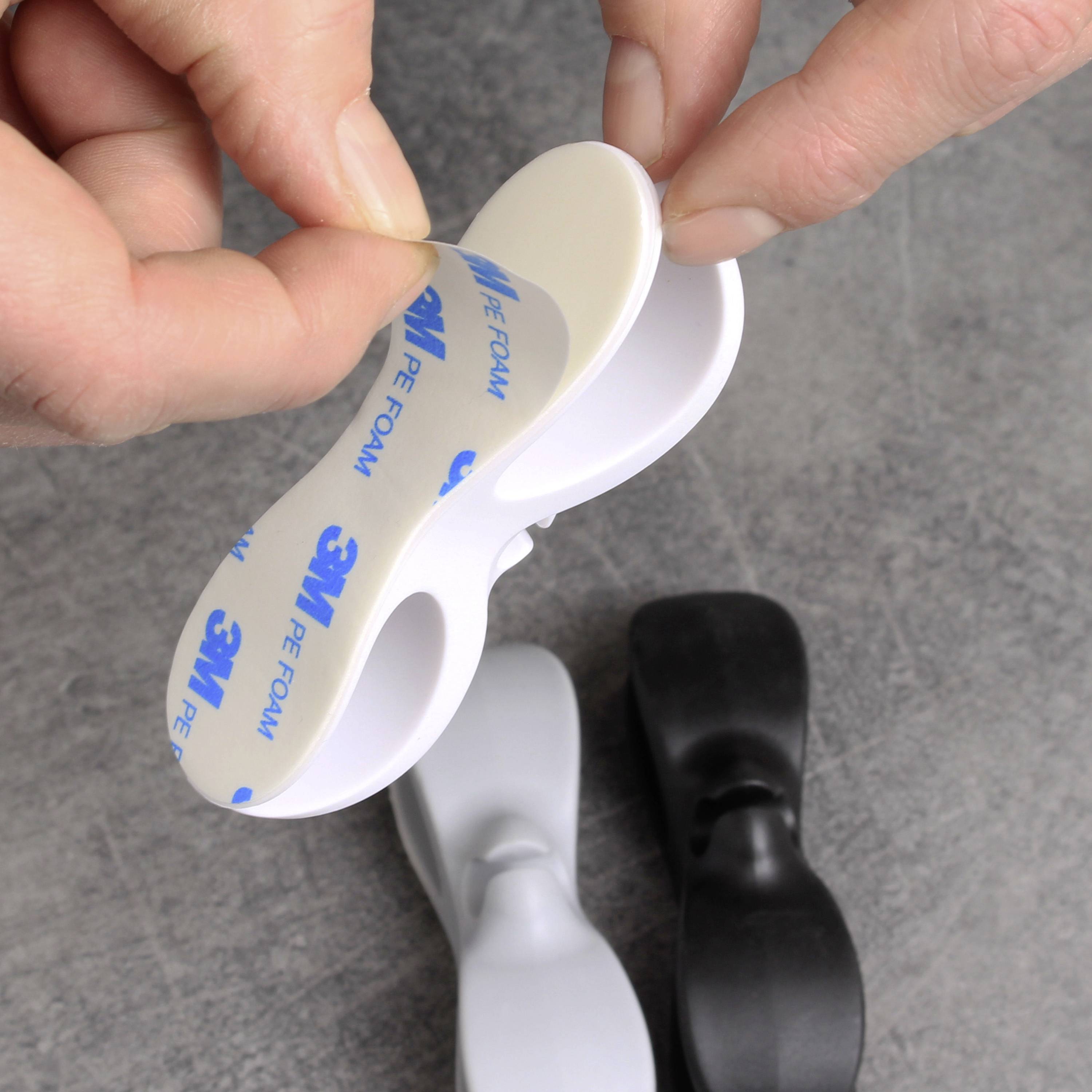 Eine Hand hält ein ovales, weißes 3M-Klebepad, das an einer glatten Oberfläche angebracht oder davon entfernt wird. 