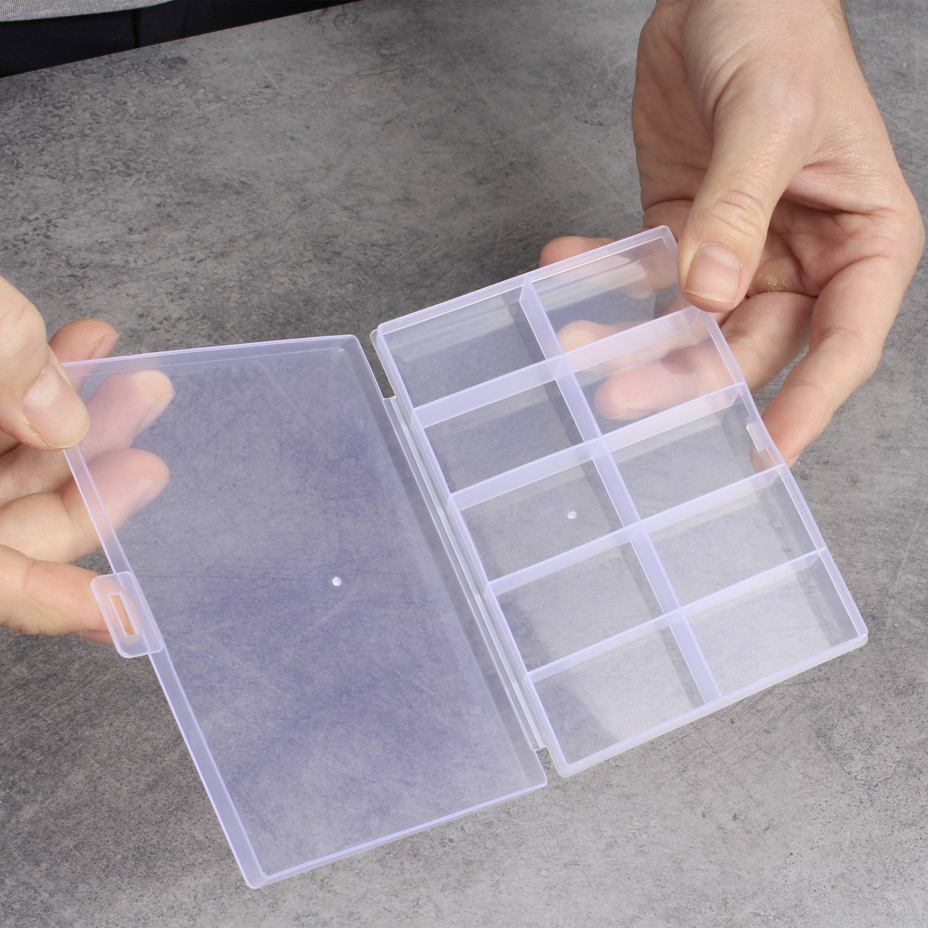 Eine Person hält eine transparente, leere Aufbewahrungsbox mit mehreren Fächern in beiden Händen. Die Box ist offen und sichtbar.