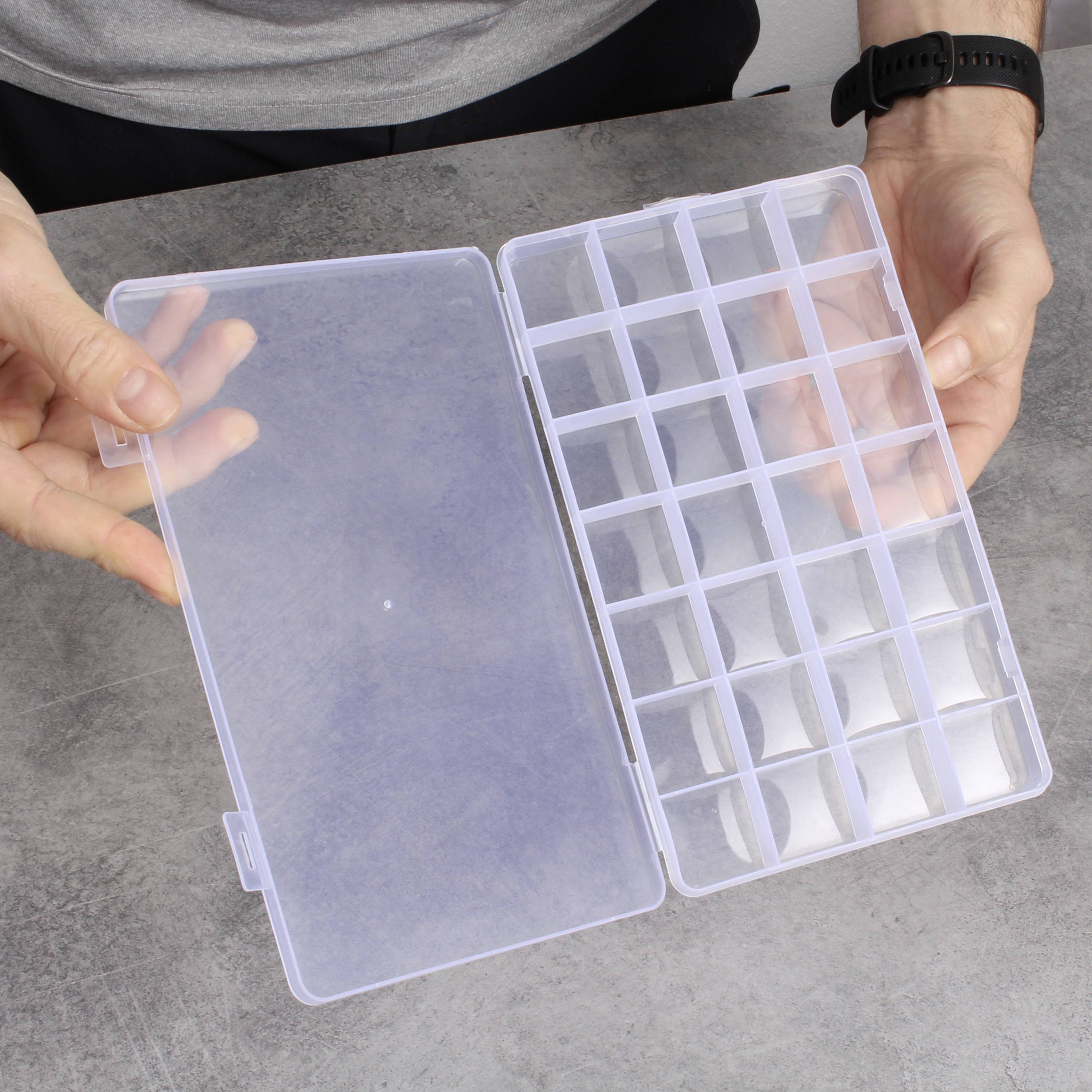Eine Person hält eine transparente, geöffnete Kunststoffbox mit mehreren kleinen Fächern in der Hand, geeignet zur Aufbewahrung von Kleinteilen.