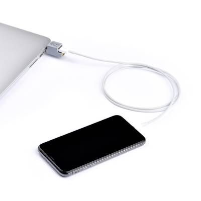 Ein Smartphone liegt neben einem Laptop, verbunden mit einem Ladekabel, das in den Laptop eingesteckt ist.