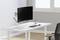 Ein schlichtes, modernes Büro mit einem weißen Tisch, darauf ein gebogener Monitor am Halter, eine Tastatur, Maus und Stiftehalter.